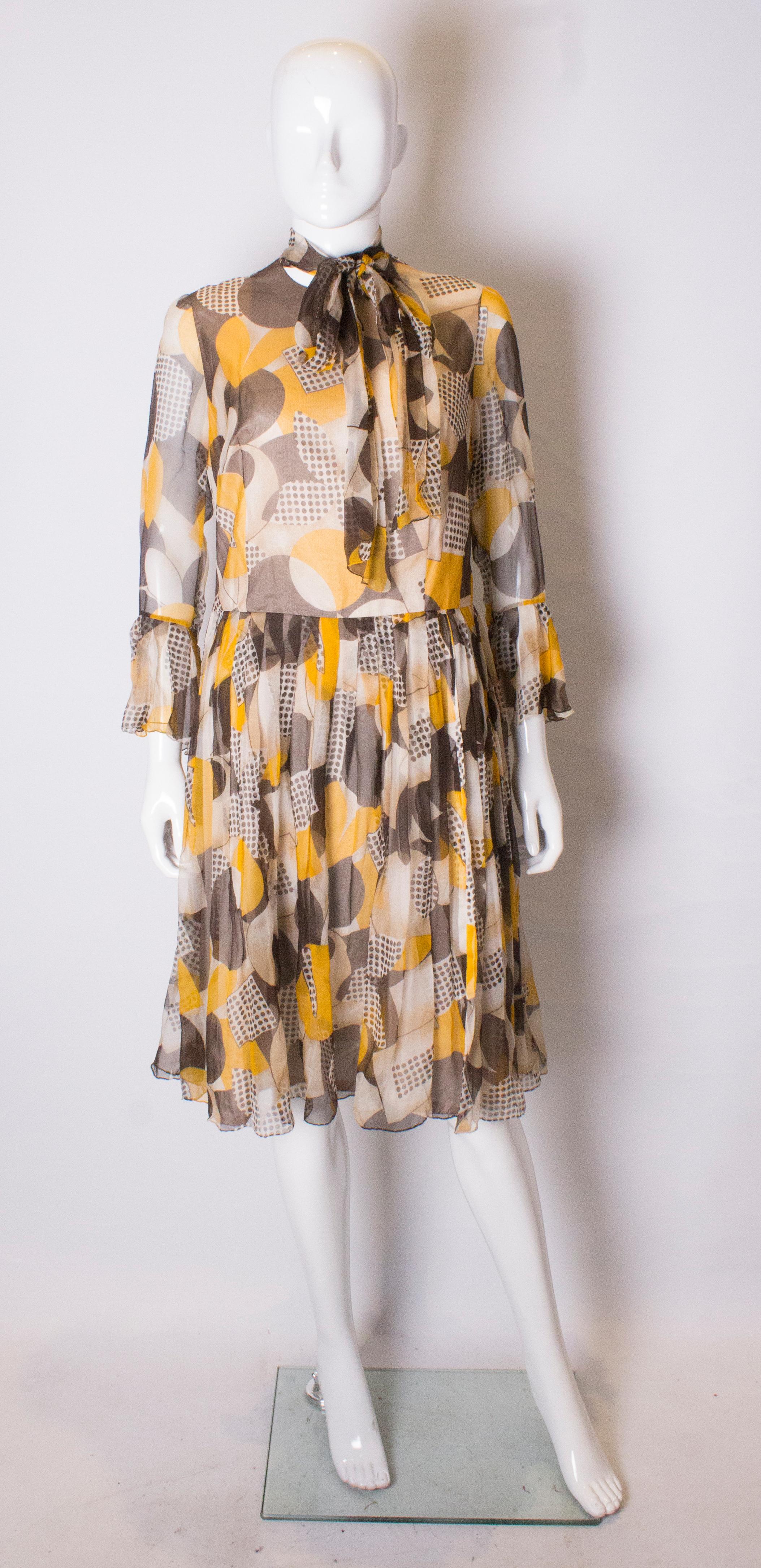 A chic cocktail dress in a groovy print of brown, yellow and cream. The dress has a tie neck , frills at the cuffs and a central back zip . It is fully lined.