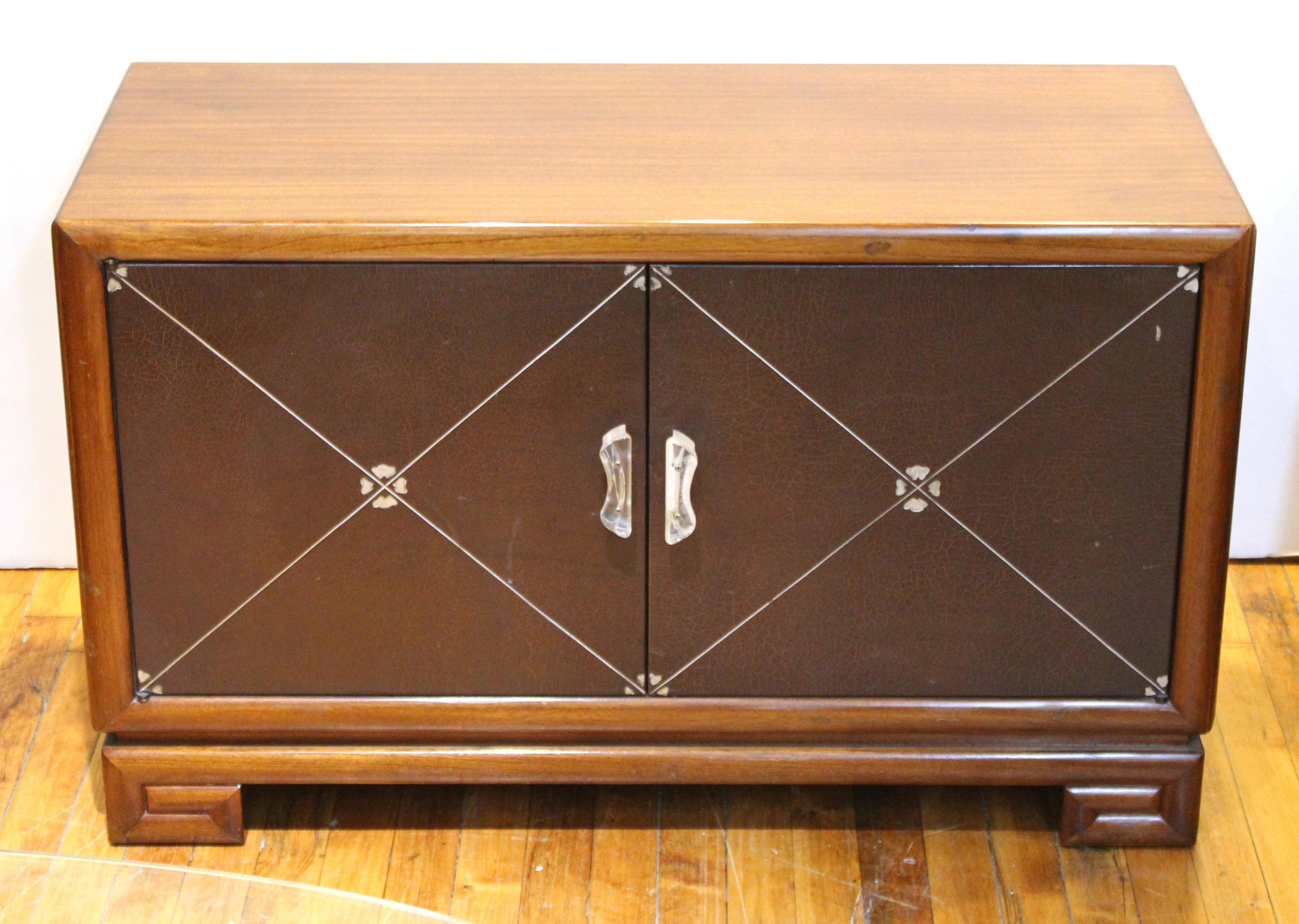 Art Deco low cabinets or nightstands in polished mahogany wood produced in the circa 1940s by Grosfeld House. The pair has silver-embossed leather double doors with Lucite handles and decorative round Lucite handles on the sides, atop Greek key form