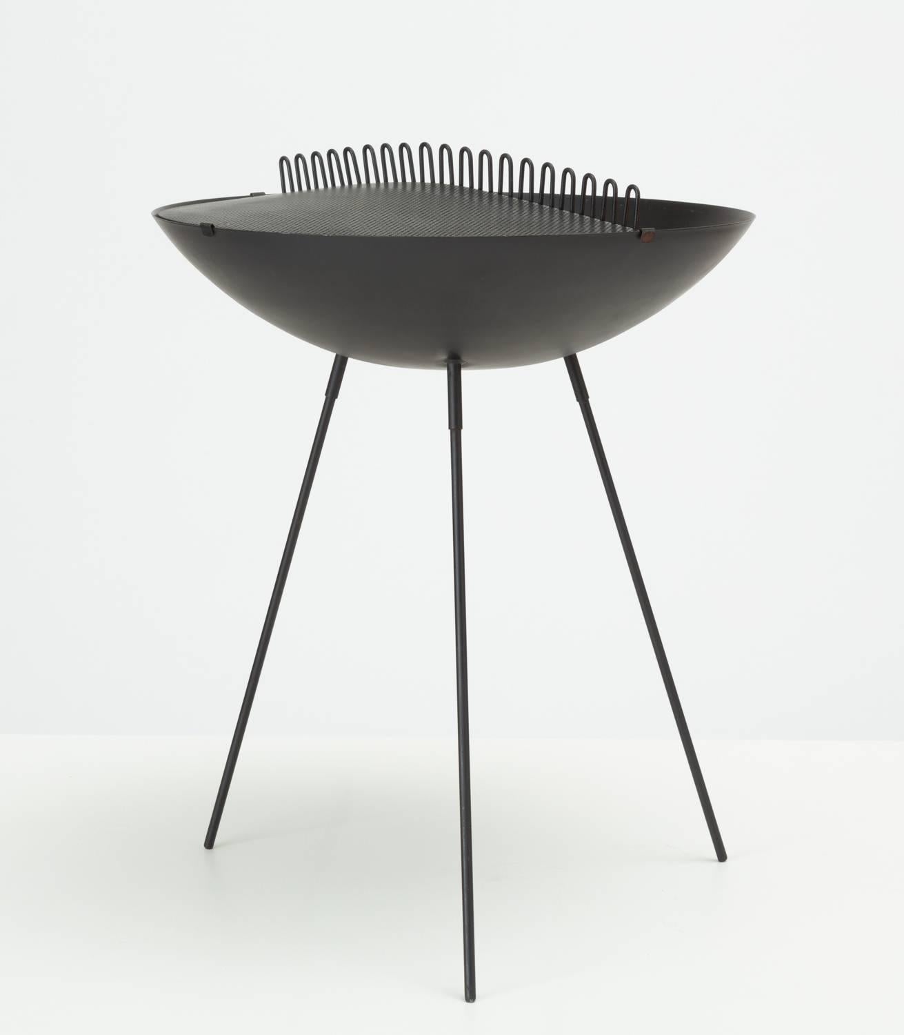 San Francisco based designers Gross and Esther Wood were especially known for their designs in perforated steel. This example is a large, bowl-shaped ashtray atop three slender legs. The piece has a partial lid of perforated steel with a wire