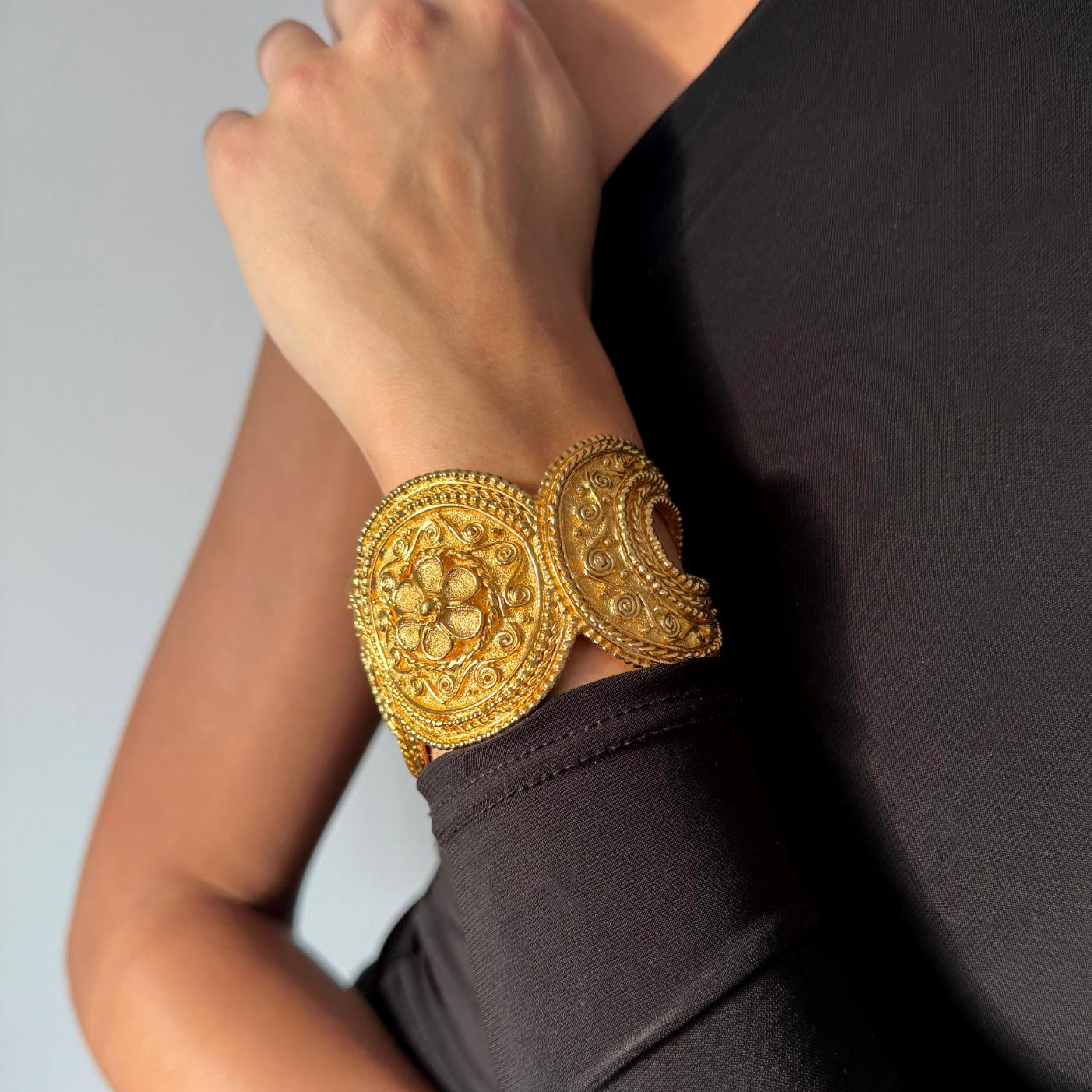 A vintage Grosse for Christian Dior gold-plated bangle bracelet from the 1980s, featuring bold circular panels with intricate floral and scrollwork designs. A striking statement piece of collectible Dior costume jewellery.

Dimensions –
7.2 cm x 6