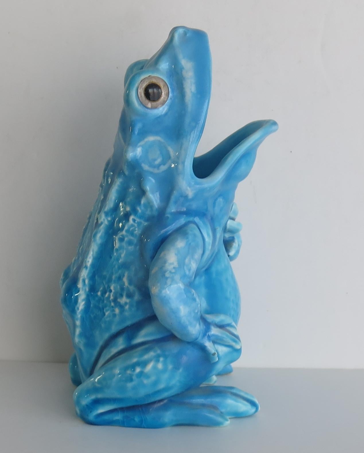 This is a pottery Spoon Warmer modelled as a Bull Frog, in the style of Burmantofts Art Pottery, England, dating to the late 19th century.

This grotesque animal sculpture is modelled as a scaly Bull Frog, covered in a blue/turquoise glaze and