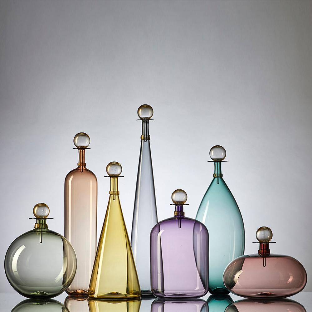 Set of 7 contemporary hand blown glass bottles in an array of smoky colorful forms inspired by geometric decanters of Mid-Century Modern design. Coordinated neck-wrap and blown glass stopper finish each decanter with luminous gold-leaf. Offered in a