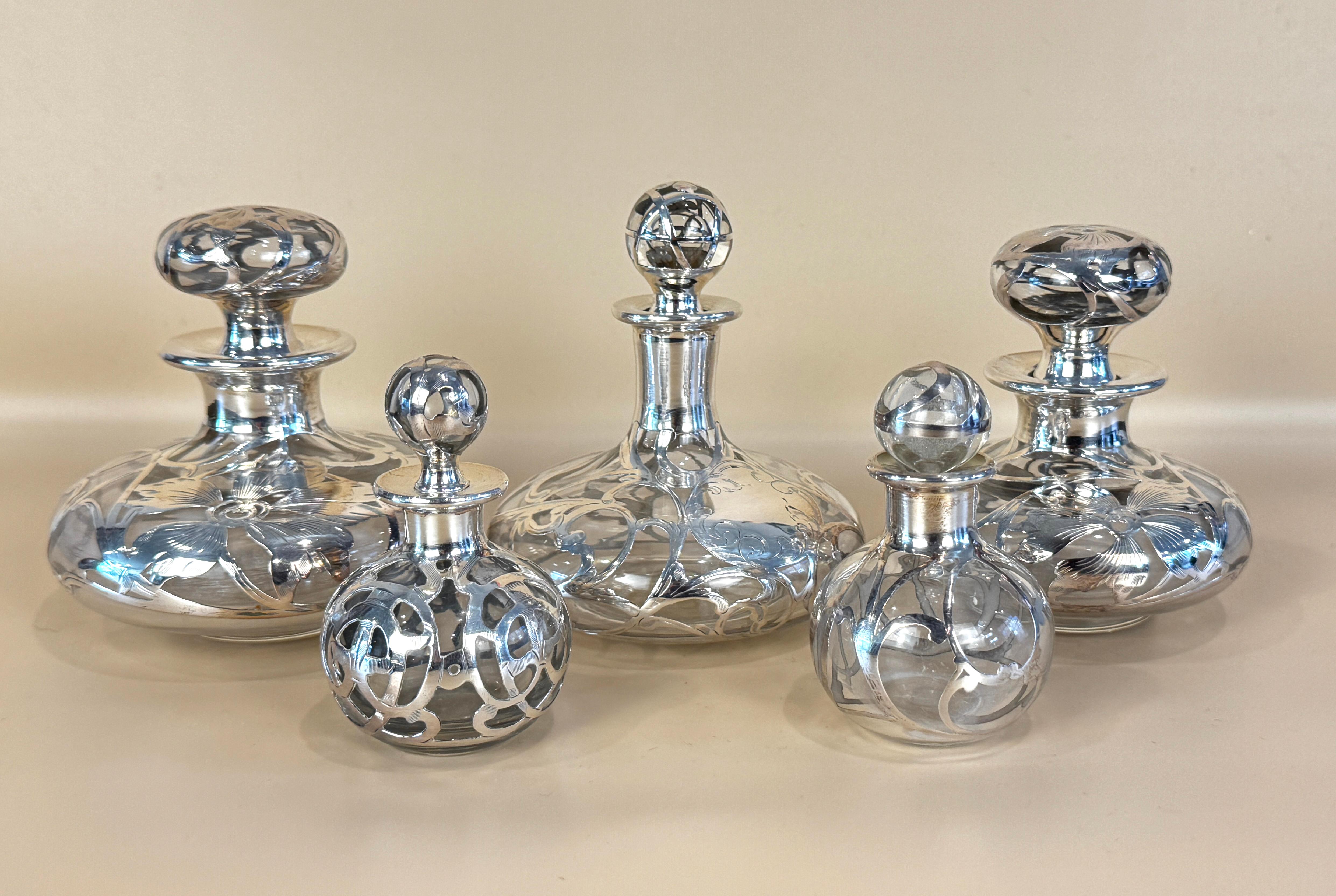 Groupe de cinq anciens flacons à parfum en verre recouvert d'argent, chacun avec un bouchon en argent. Comprenant trois bouteilles plus grandes, chacune avec une large base et un recouvrement d'argent sous forme de délicates vrilles feuillagées