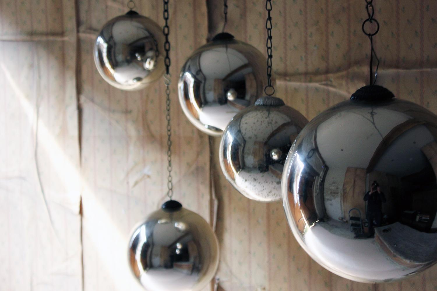 The group of five hand-blown lustrous mercury glass witches balls of silver colour and mixed sizes, three particularly large, having the original hanging pressed loop crown attachments, and when hung each reflecting an entire room, the wholes