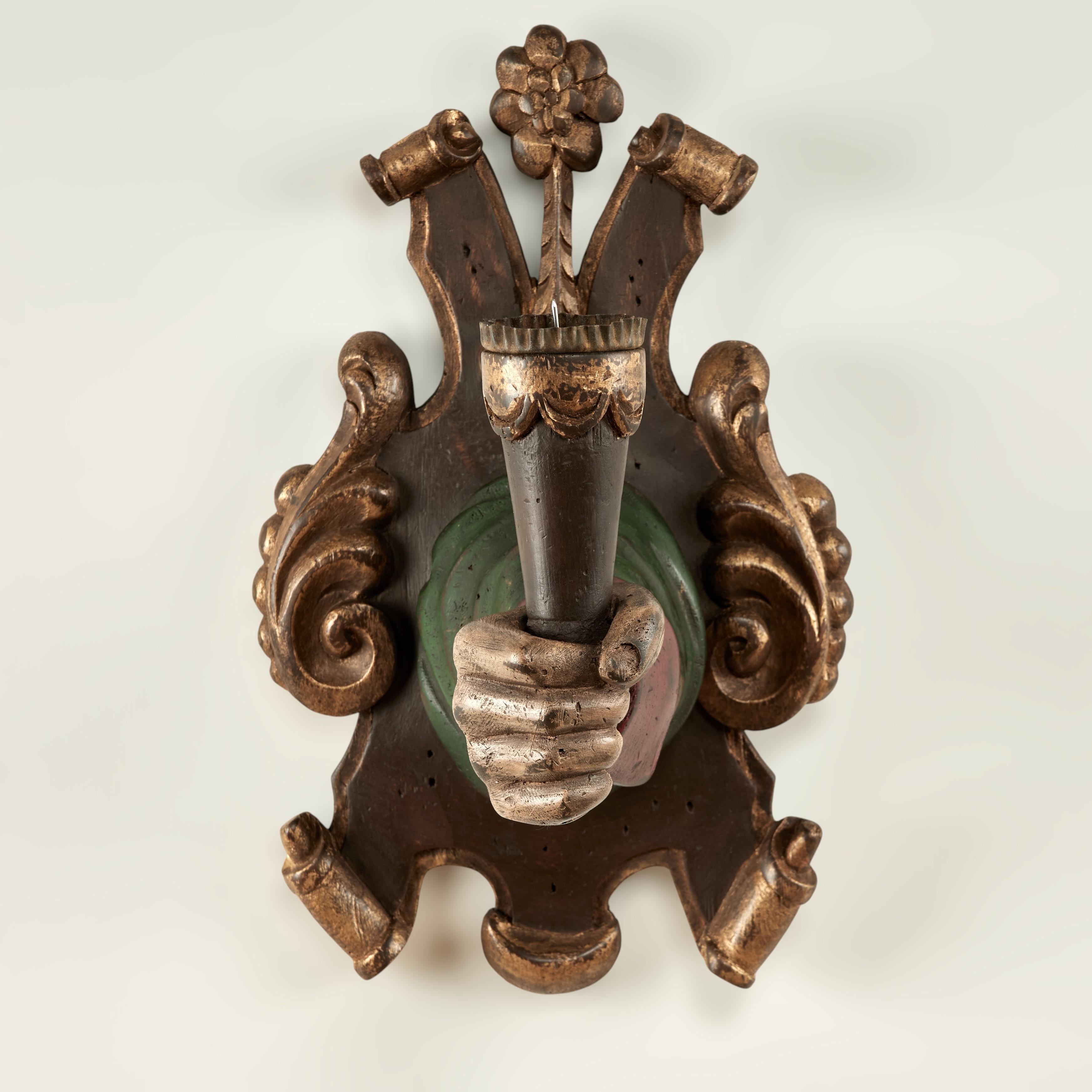 Rare and remarkable group of four antique Italian wall sconces carved from a hardwood featuring a parcel gilt coat of arms style back plate supporting a painted arm with fist holding a torchiere and corrugated tin candle cup.