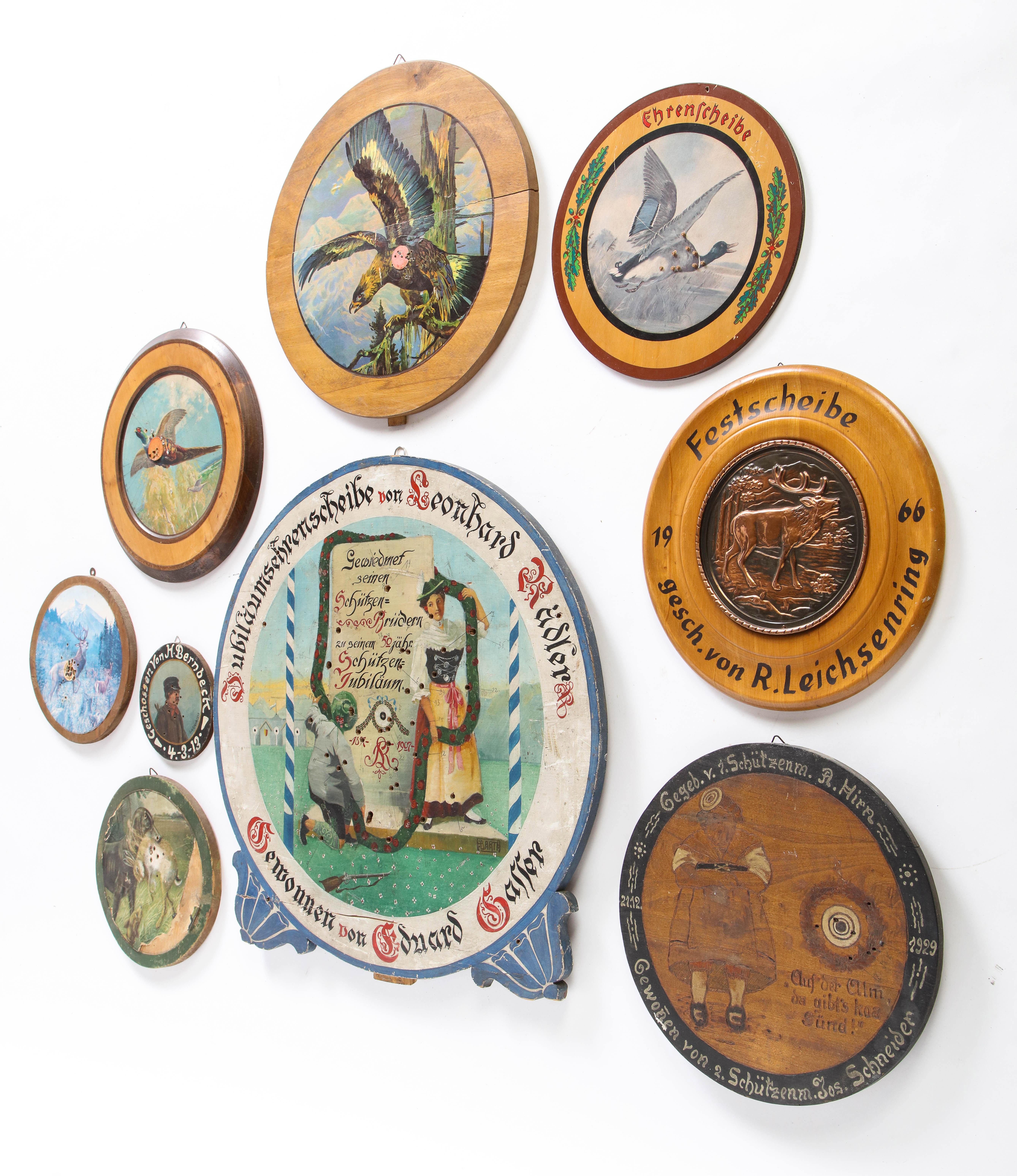 A group of nine trade signs, dart boards, marketing signs and game boards, probably Austrian, from the 20th century. All take circular form, but are of varying sizes. Each is characterized by text, avian imagery, wildlife scenes, and other