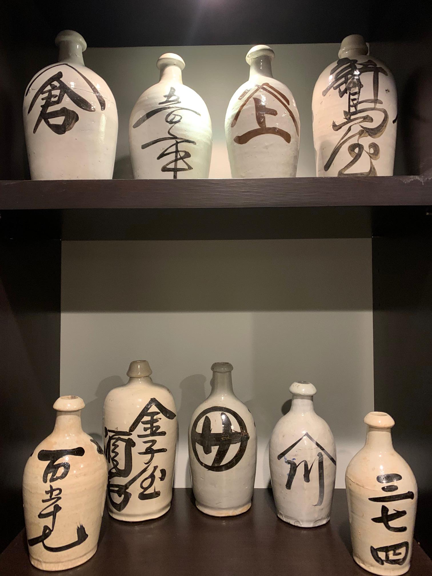 A large collection of nice Japanese stoneware sake bottles circa first quarter of 20th century. Heavily potted, these bottled were dipped in white glaze and brushed on with black Kanji characters to show the brand names of sake. They were likely