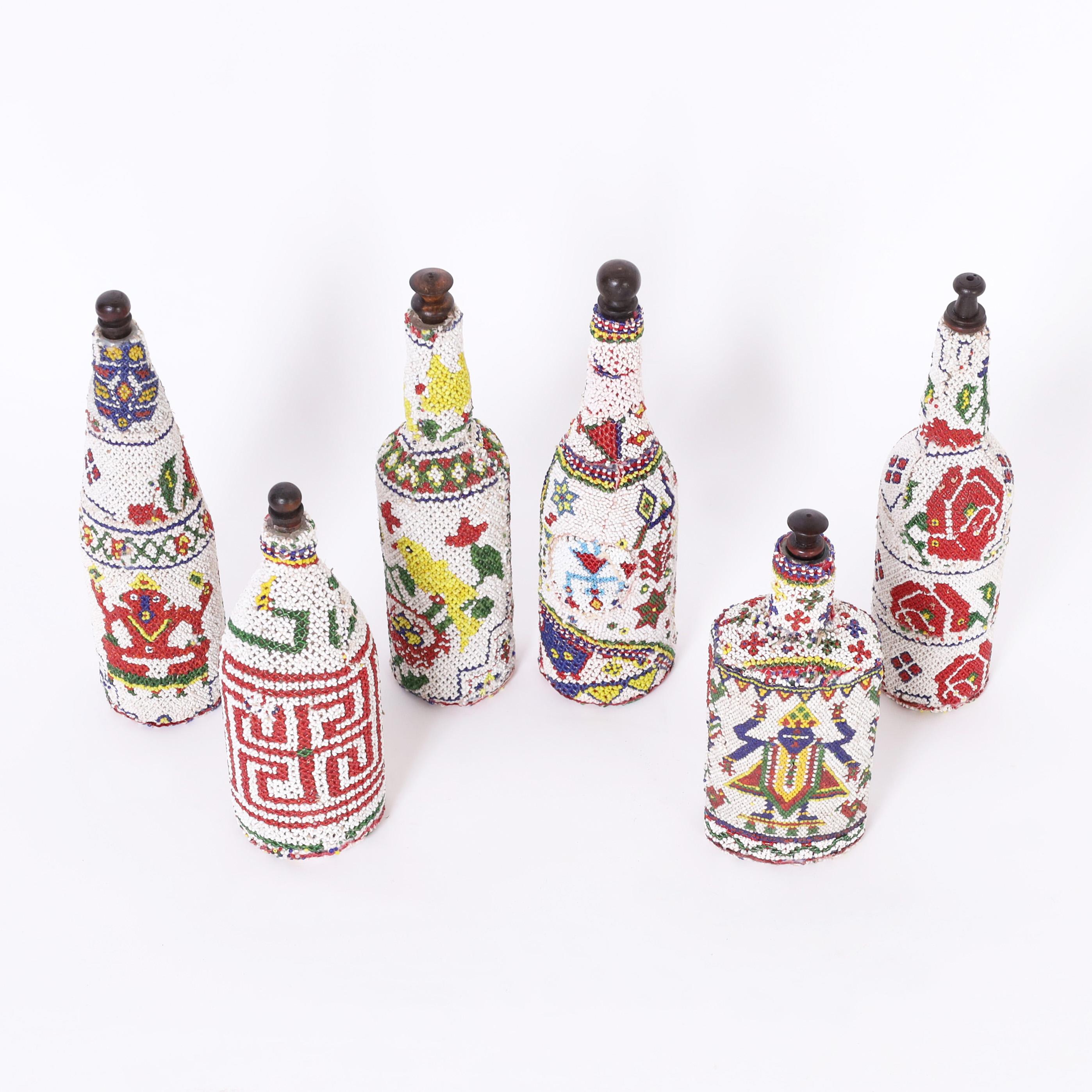 Striking group of four mid century bottles hand decorated with glass beads in bold colorful symbolic and geometric design with turned wood stoppers.

Taller Bottles: H: 13 DM: 3.5 $1,175.00 *Two center bottles are SOLD
Smaller Bottle on left: H: 11