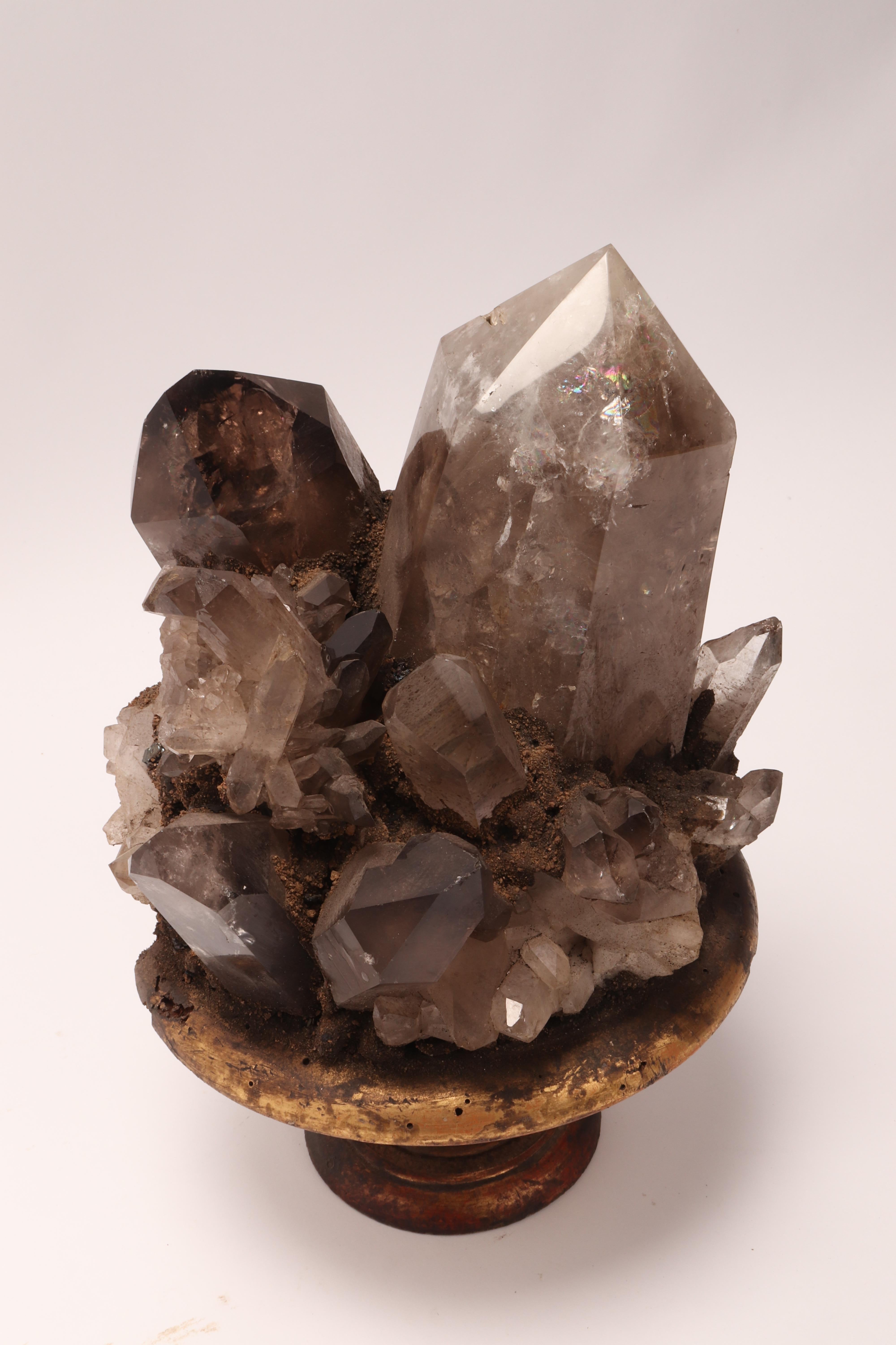 A natural mineral specimen for Wunderkammer: a big group of smoke crystal quartz mounted on a carved wooden base gold gilt on a shape of a vase. Italy, circa 1880.