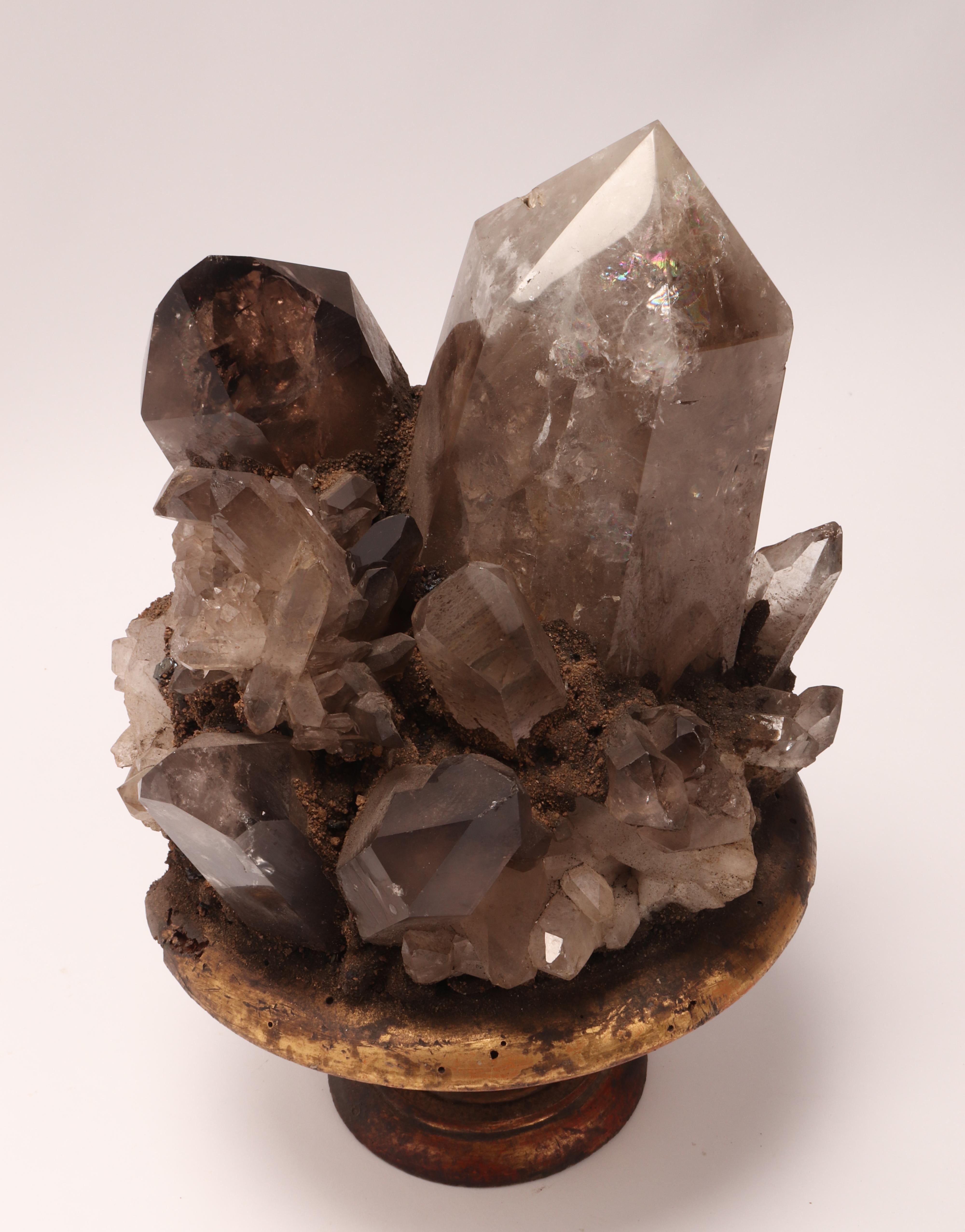 A natural mineral specimen for Wunderkammer: a big group of smoke crystal quartz mounted on a carved wooden base gold gilt on a shape of a vase. Italy 1880 ca.