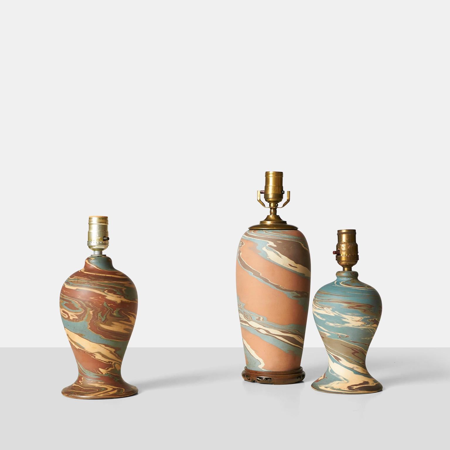 A group of 3 mission swirl style table lamps with marbled ceramic body and carved wooden base. Brass hardware, marked 