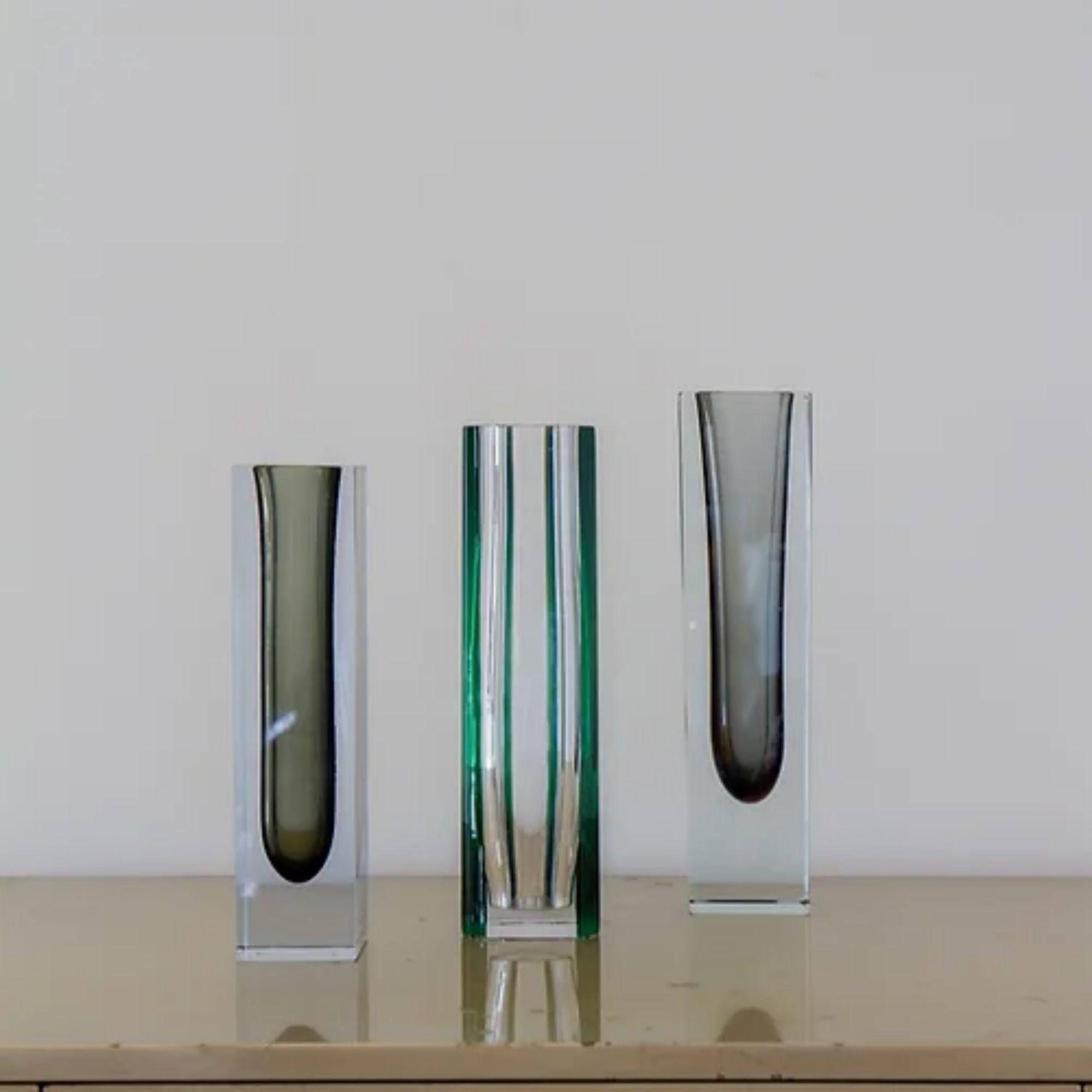A group of three large Murano vases comprising of

A large square Murano Sommerso glass vase with a charcoal centre cased in clear glass, small chip to top rim.
Measures: 25.5cms high x 6.5cms square

A unusual clear murano glass vase with