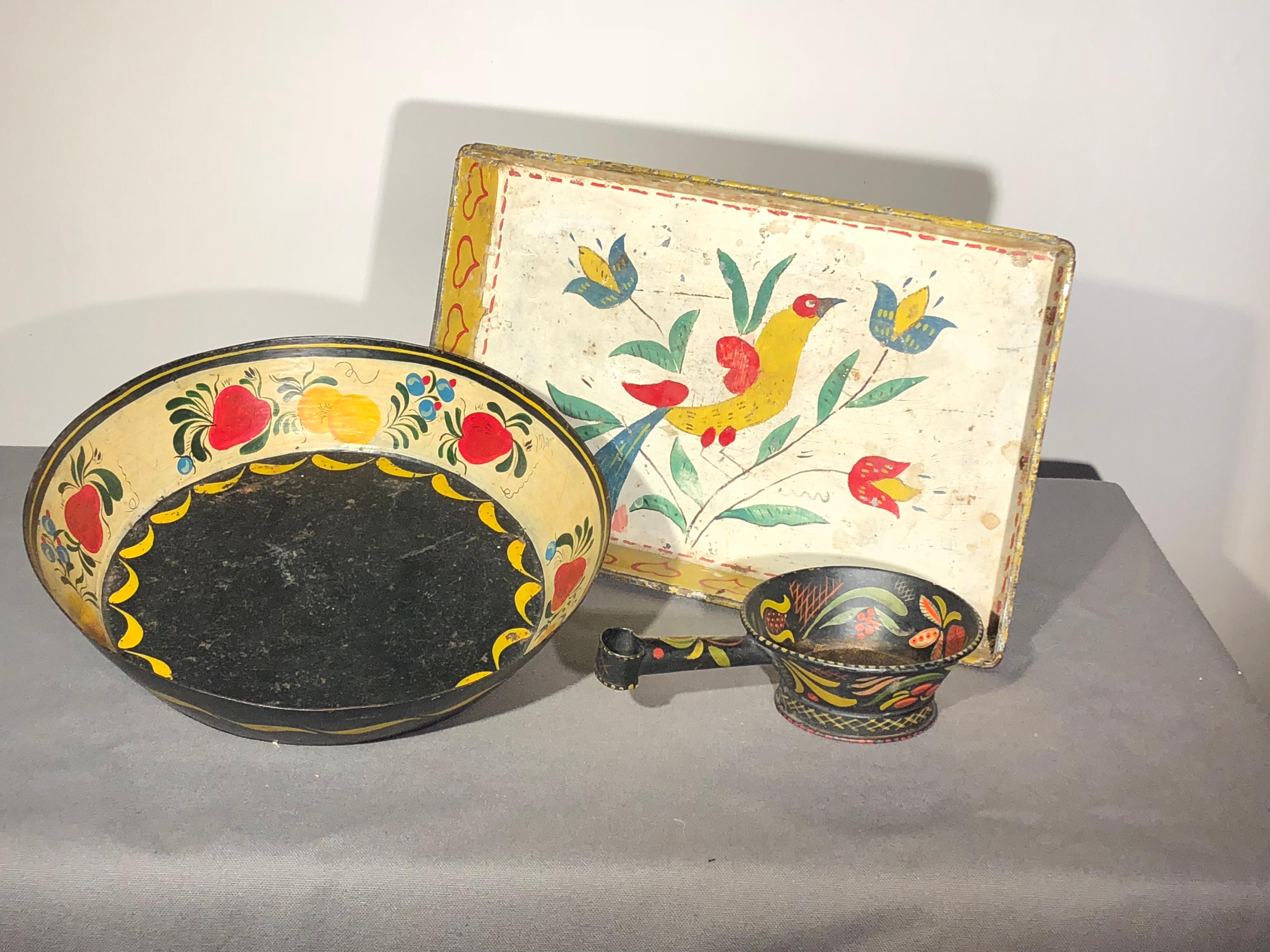 A group of 3 toleware articles including a rectangular tray decorated with birds and flowers, a circular tray in black ground with painted fruits and garlands, and a small tea strainer in black ground with painted leaves and flowers
European and