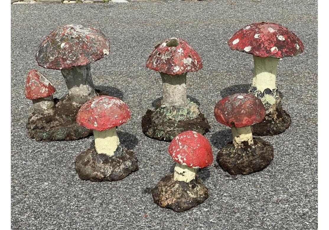 A collection of whimsical decorative cast stone Painted Garden Mushrooms. Five single mushrooms and one double, all with red painted tops, white stems and green and black textured bases. Some have white spotted tops as well. 
Various