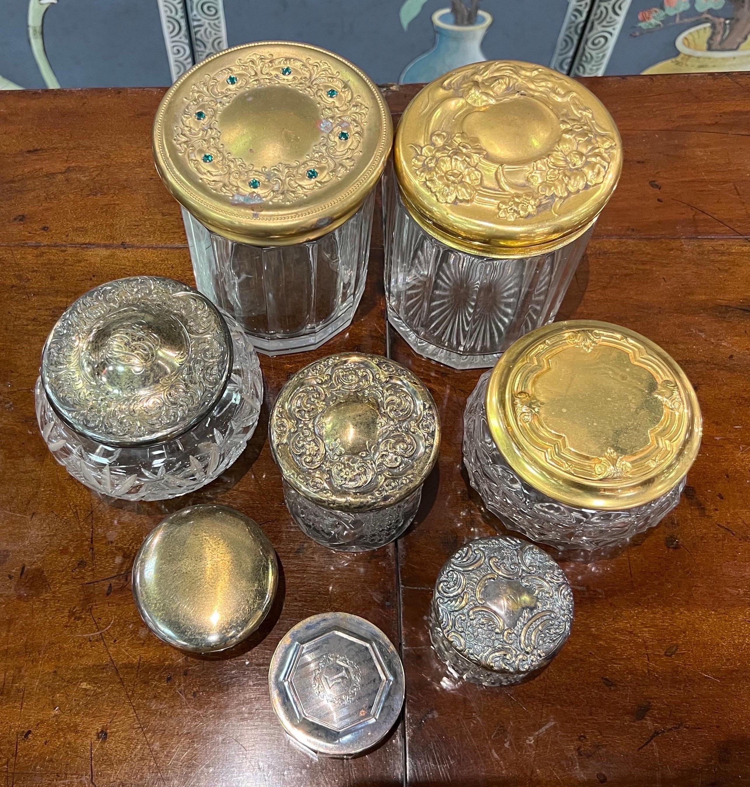 Set of 8 cut glass jars- some with pressed brass lids, some with silver lids. A few of the silver ones are marked with hallmarks. One of the grass lids is encrusted with jewels. 

Dimensions listed is largest.