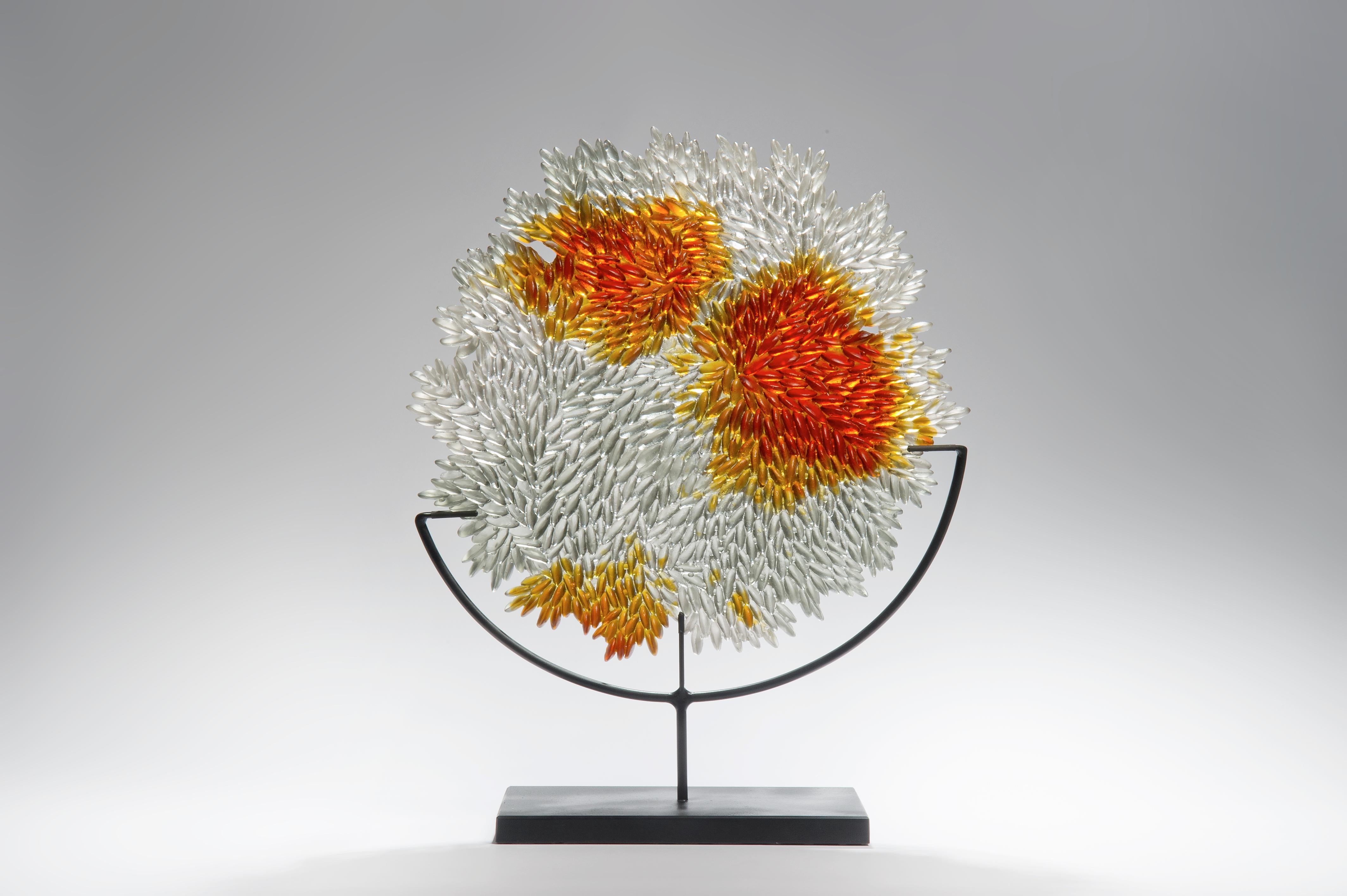 Grown Round is a unique textured mounted glass sculpture in clear & amber by the British artist Nina Casson McGarva. The piece comes with a black steel stand.

Casson McGarva firstly casts her glass in a flat mould where she introduces all of the