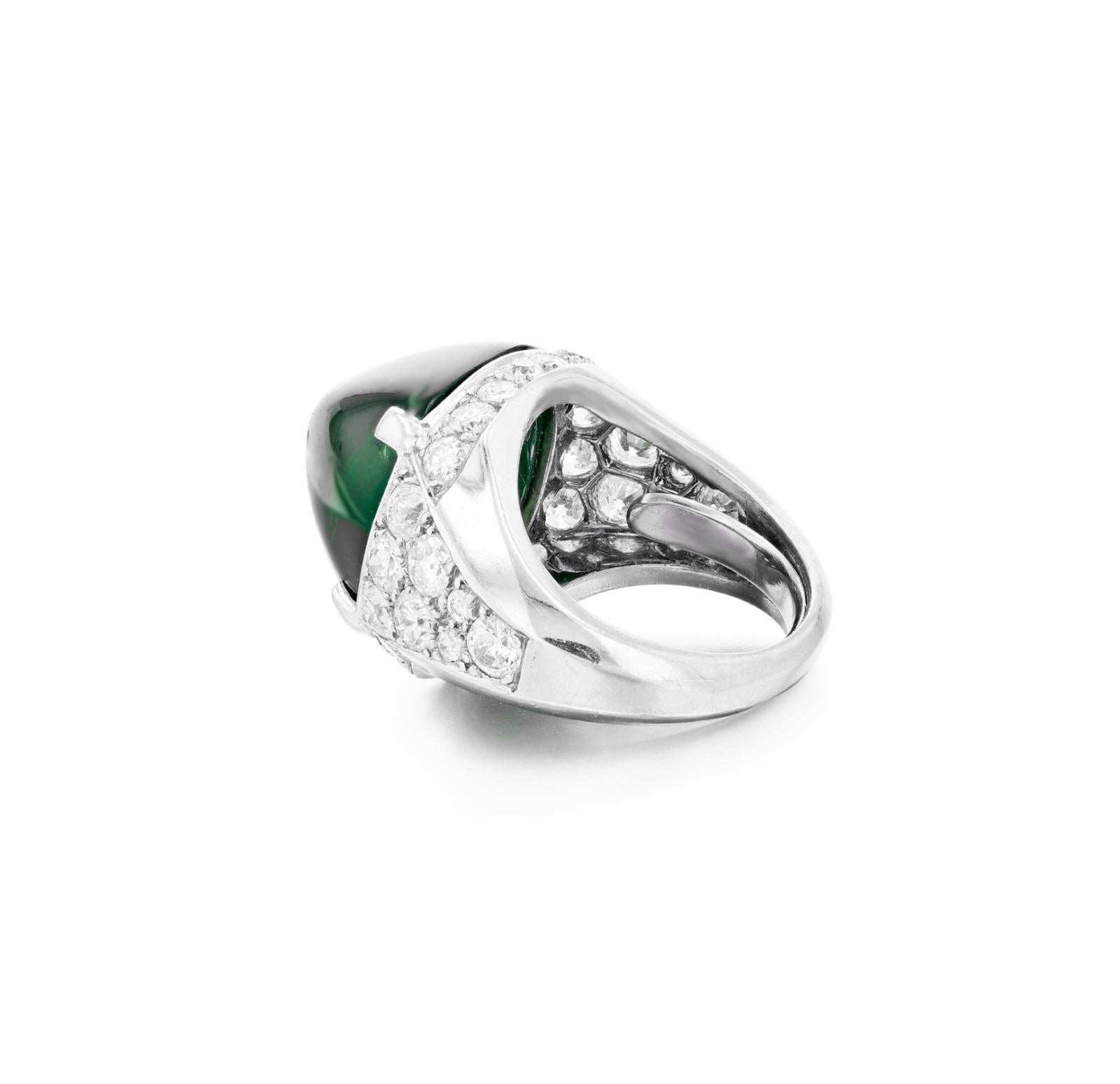 This exquisite ring features a striking 21-carat sugarloaf-shaped cabochon emerald as its centerpiece. The vivid green gemstone is gracefully set in an elegant mounting that is further enhanced by a halo and accents of brilliant-cut diamonds, adding