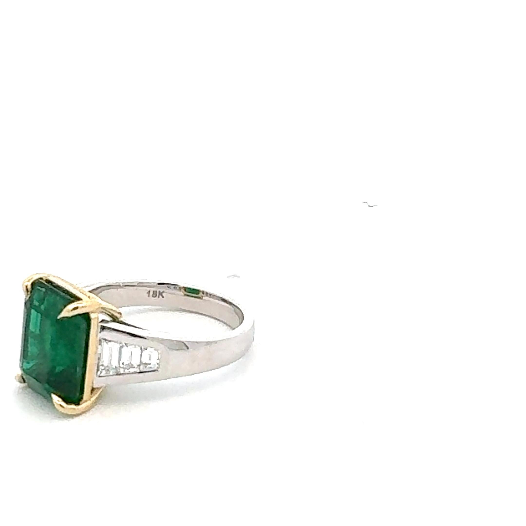 This ring displays a GRS certified 5.60 carat Zambian emerald set in 18 carat white and yellow gold, flanked by tapered shaped  diamonds 0.66 carat. The emerald has a elongated cut, emphasizing its deep luster green color.  Overall, it’s an elegant