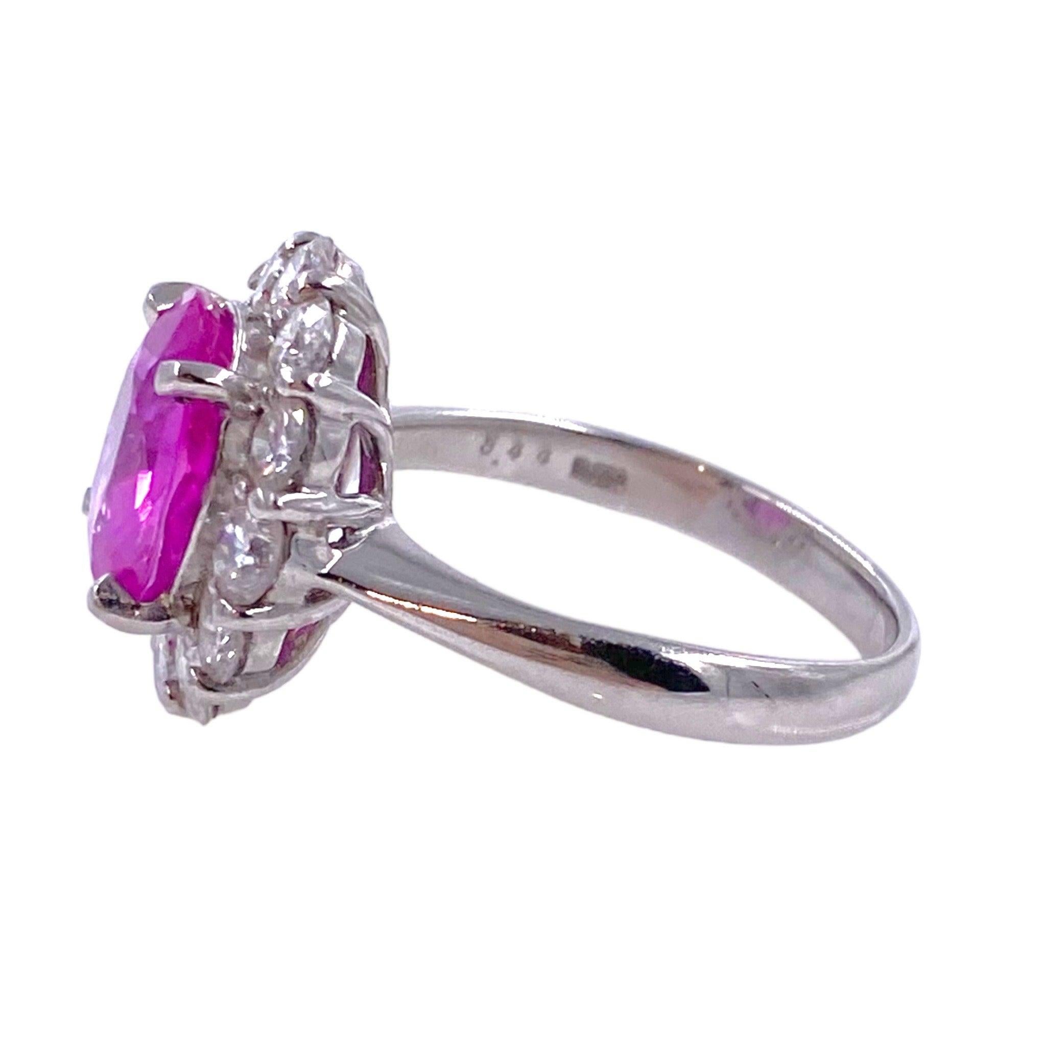Der aus Platin gefertigte Ring zeigt einen ovalen rosa Saphir-Solitär, der von Diamanten umrahmt ist. Das Design ist schlicht und elegant. Der Kontrast zwischen der Farbe des Mittelsteins und der Diamanten unterstreicht die Schönheit des Rings.