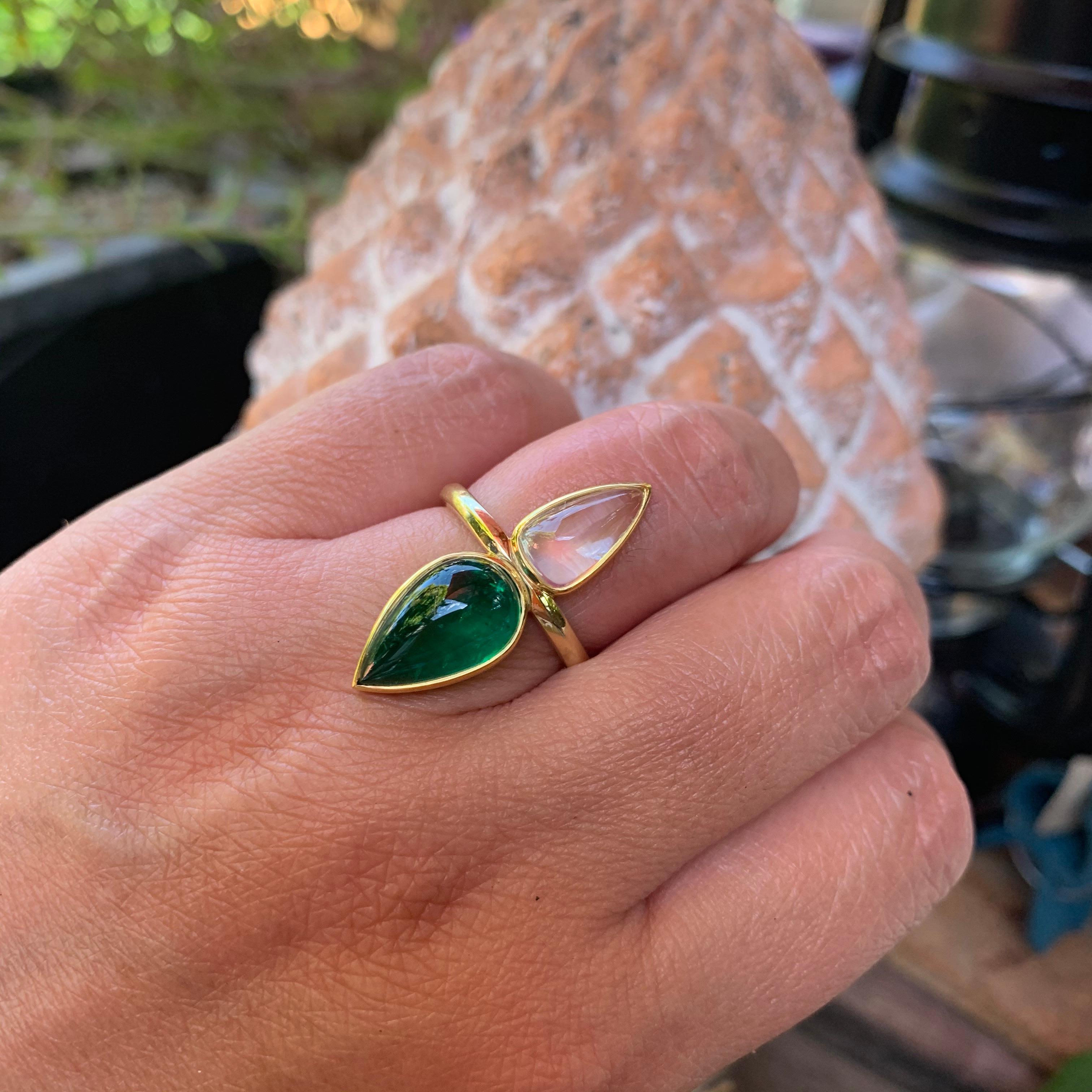 This ring features a 4.46 carat fine pear shaped Colombian emerald cabochon and exceptionally clear 2.3 carat rainbow moonstone from Madagascar. These two elements are brought together in this hand forged 22/18 karat Fairmined gold ring  by our