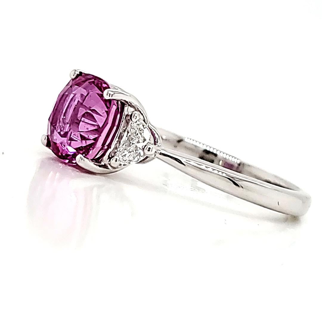 Certified by GRS, this exquisite ring features a rare 2.32 cts cushion vivid pink sapphire, sourced from the enchanting lands of Madagascar. 

Heated to perfection, its dazzling color radiates warmth and charm.

Accentuating the center stone are two