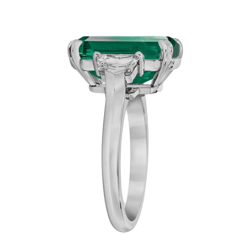 a breathtaking masterpiece: a 9.17 carat natural emerald, certified as insignificant oil, radiating with unparalleled beauty. 

This exquisite gemstone is elegantly set in a solid platinum ring, flanked by two stunning trillion-cut diamonds, each