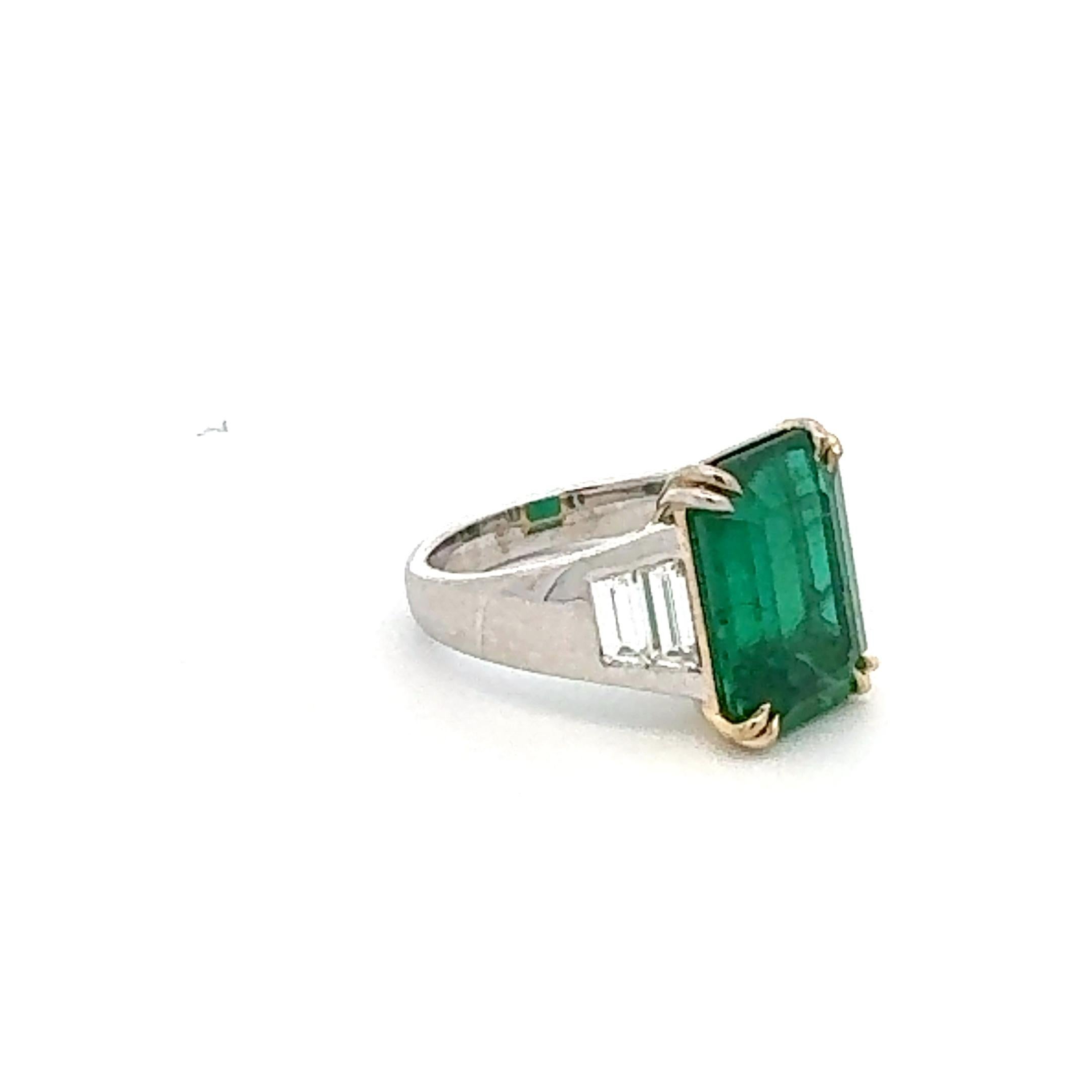 This ring displays a GRS certified 6.05 carat Zambian emerald set in 18 carat white and yellow gold, flanked by tapered shaped diamonds 0.72 carat. The emerald has a elongated cut, emphasizing its open green color. Overall, it’s an stunning and