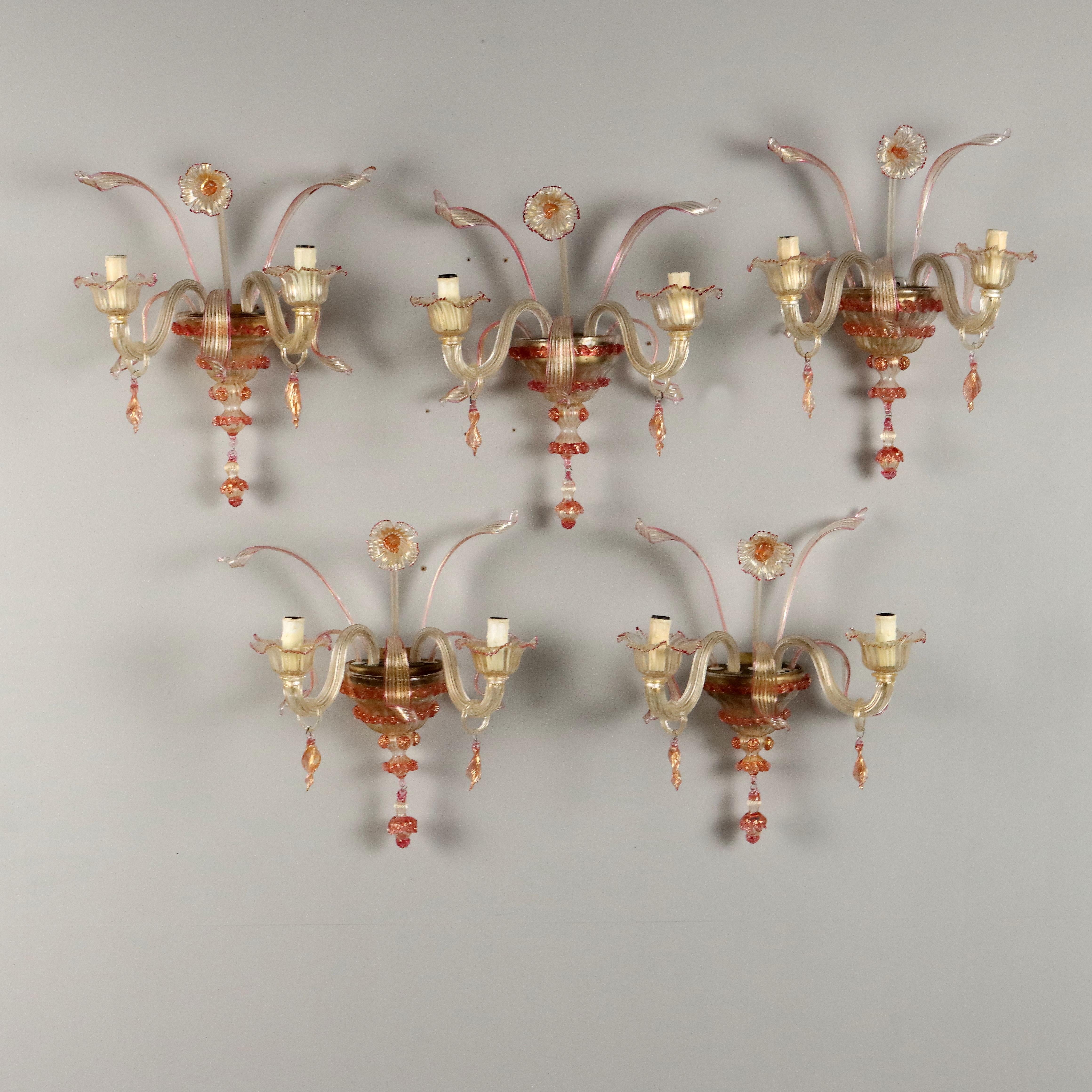 Gruppo di cinque applique a due luci in vetro soffiato di Murano, XX secolo. Decorazione composta da fiore, foglie e pendenti. Una delle applique presenta piccolo sbecco nella sezione inferiore.