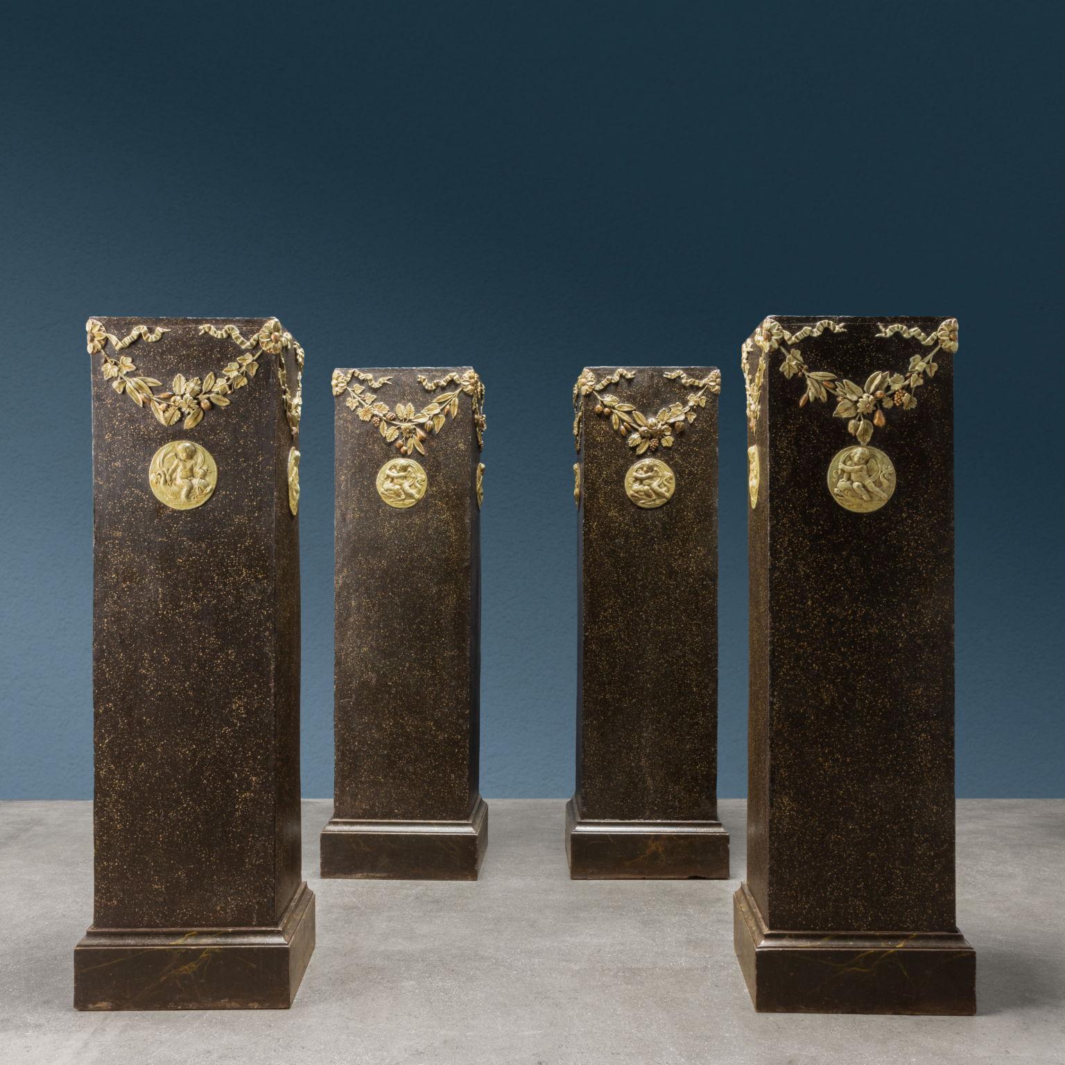 Groupe de quatre colonnes à base carrée, en bois de peuplier laqué avec un effet marbré imitant le porphyre, décoré de sculptures en pastille, laquées et rehaussées d'or. Aux quatre coins supérieurs de chaque colonne, des rosettes sculptées