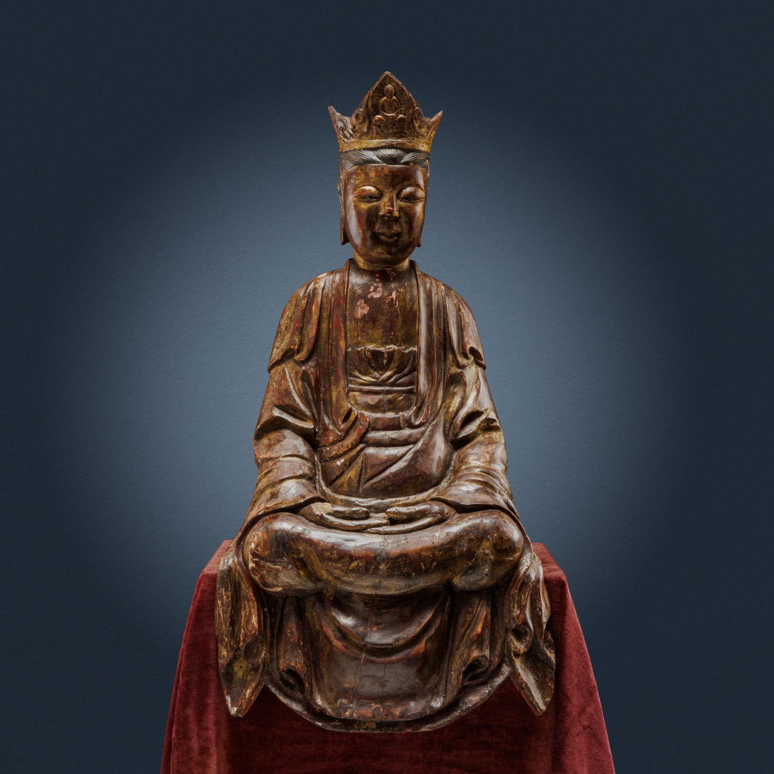 Sculpture in carved and lacquered wood with traces of gilding. Guanyin represented with crossed ankles and hands in the dhyana mudra position. Her face is shown with a serene expression, surmounted by a crown representing a Buddha. An elegant