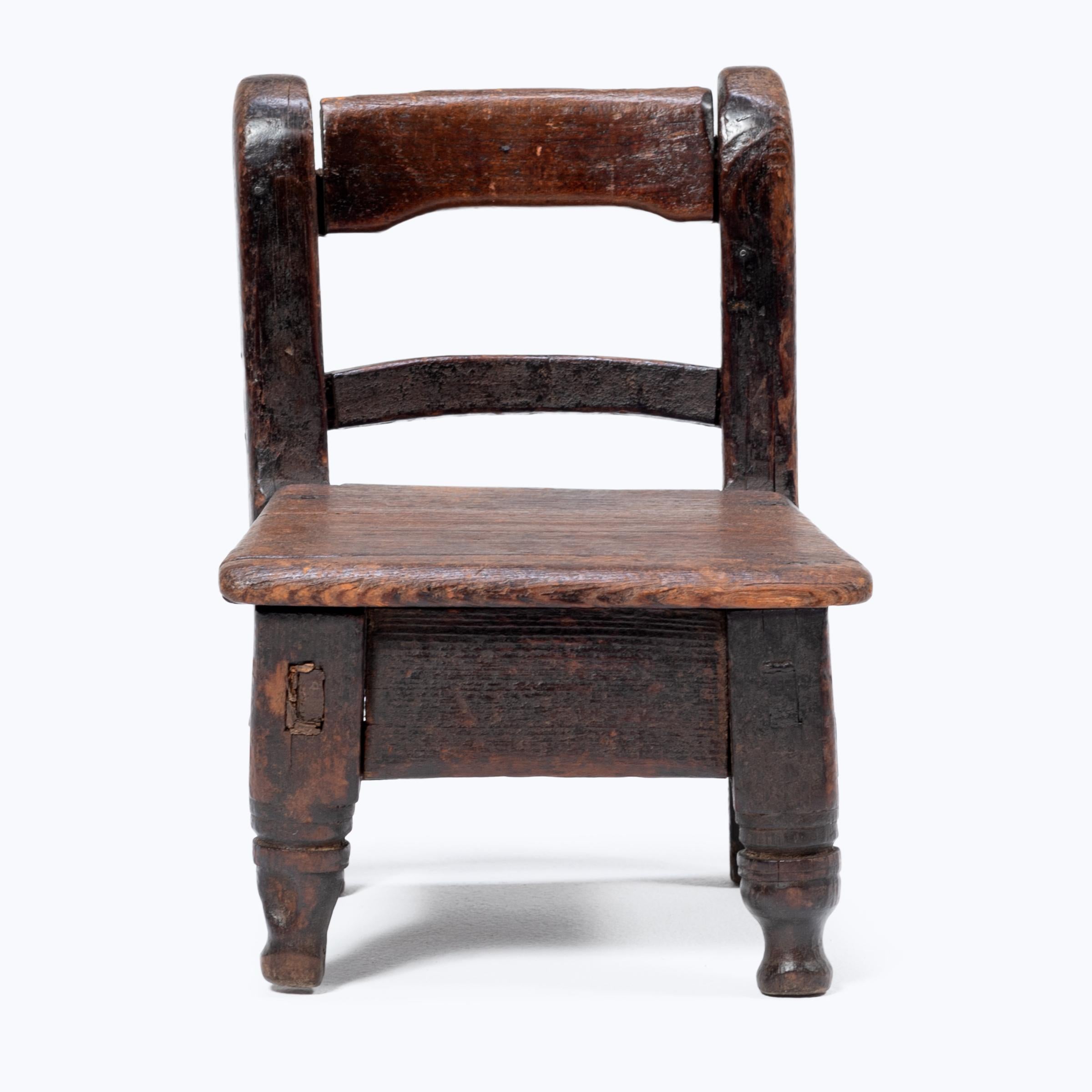 Crafted in the early 20th century, this petite Guatemalan children's chair charms with its playful asymmetry and richly textured surface. Influenced by Spanish Colonial furniture design, the chair has a slatted back and square seat resting on two
