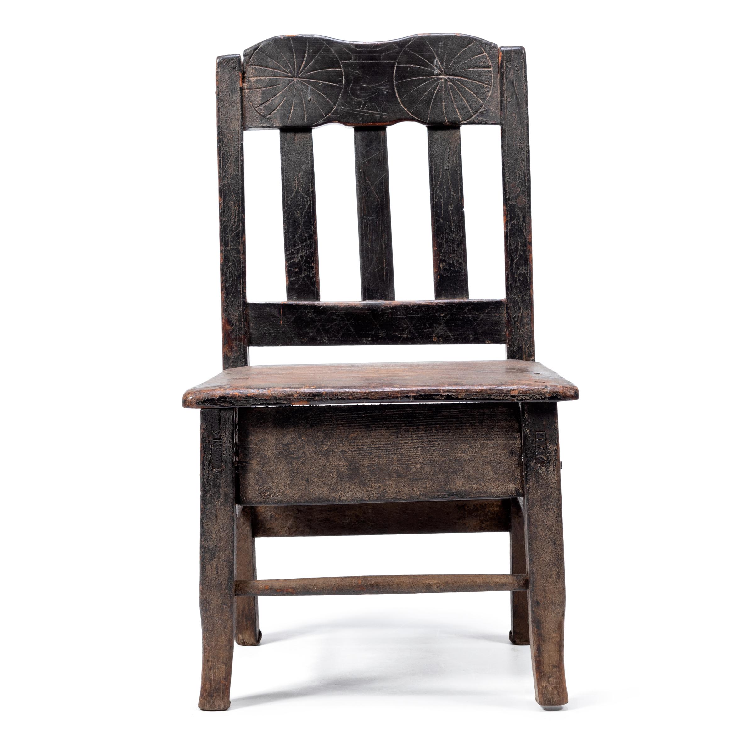 Crafted in the early 20th century, this petite Guatemalan children's chair charms with its playful asymmetry and richly textured surface. Influenced by Spanish Colonial furniture design, the chair has a slatted back carved with abstract patterns and