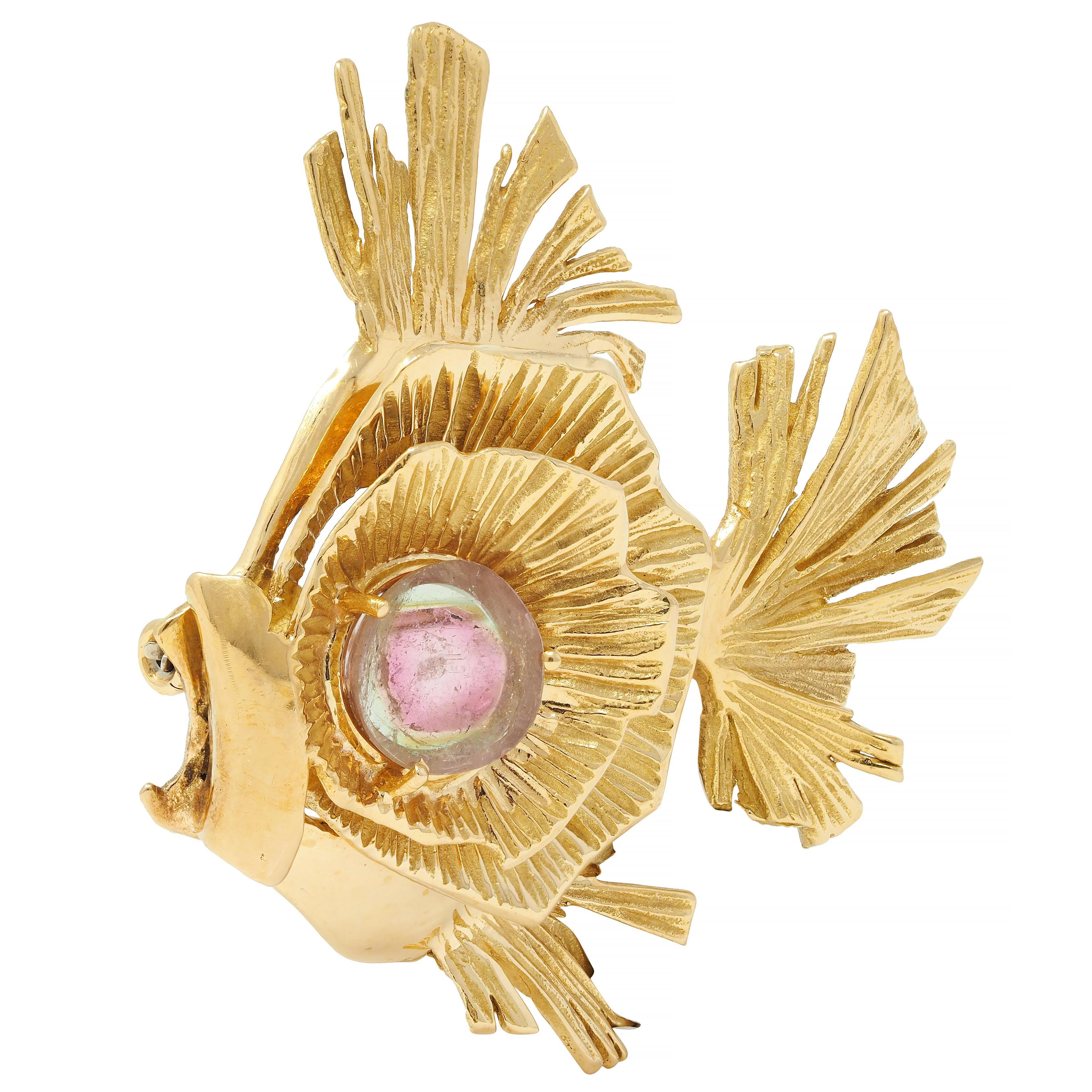 Designed as a stylized tropical fish with dimensionally pleated fins 
Featuring a 18.0 mm round tablet of watermelon tourmaline
Transparent colorless, medium pink, and light green in color
Prong set as eye centered on tiered dimensional rings 
With
