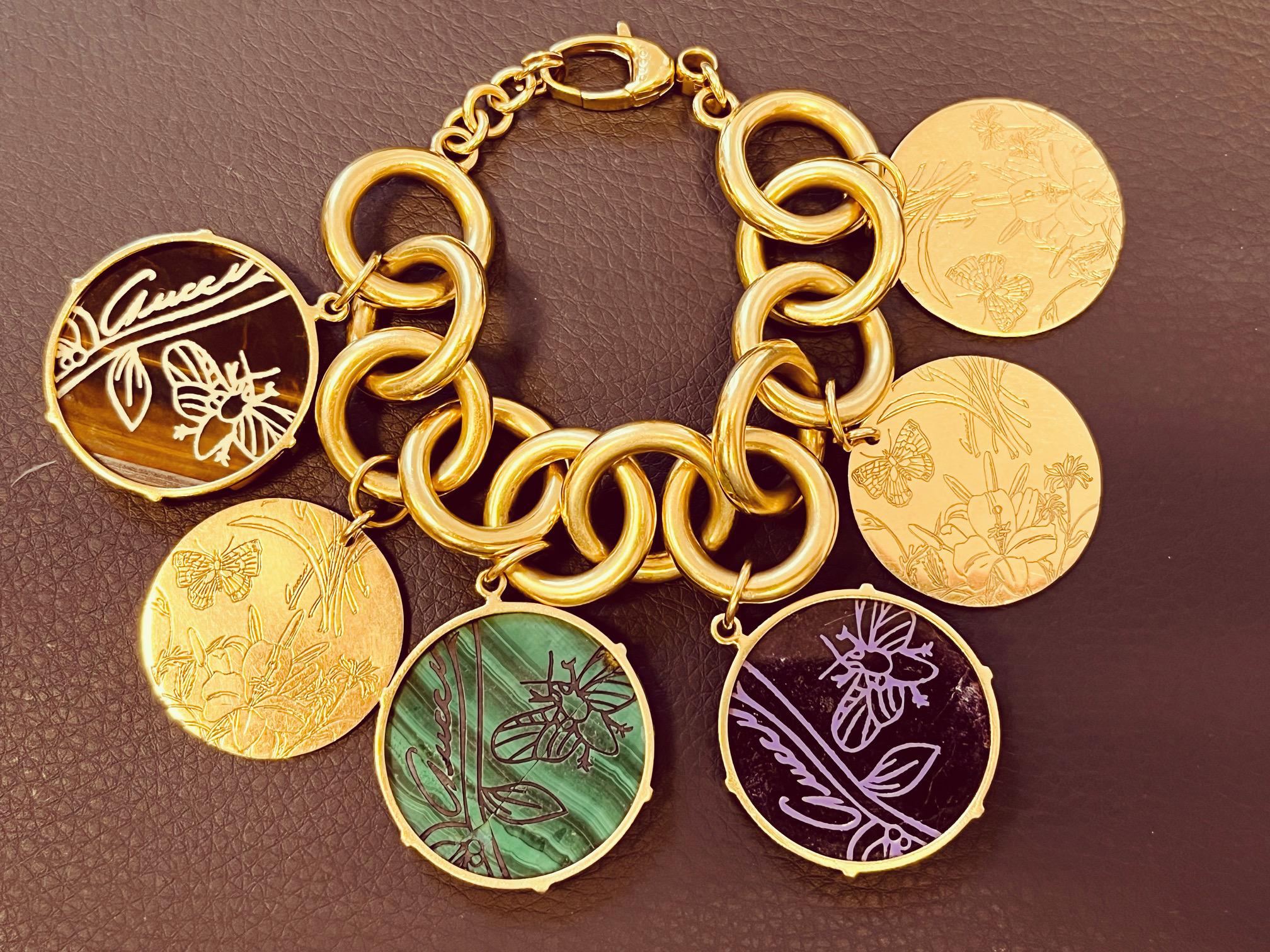GUCCI - A Gucci Flora St. Tropez 18ct yellow gold bracelet with Malachite, Sugilite, Tiger's Eye, and gold etched charms. The bracelet is designed with circular links, and has a total of six discs hanging from the links with etchings of butterflies