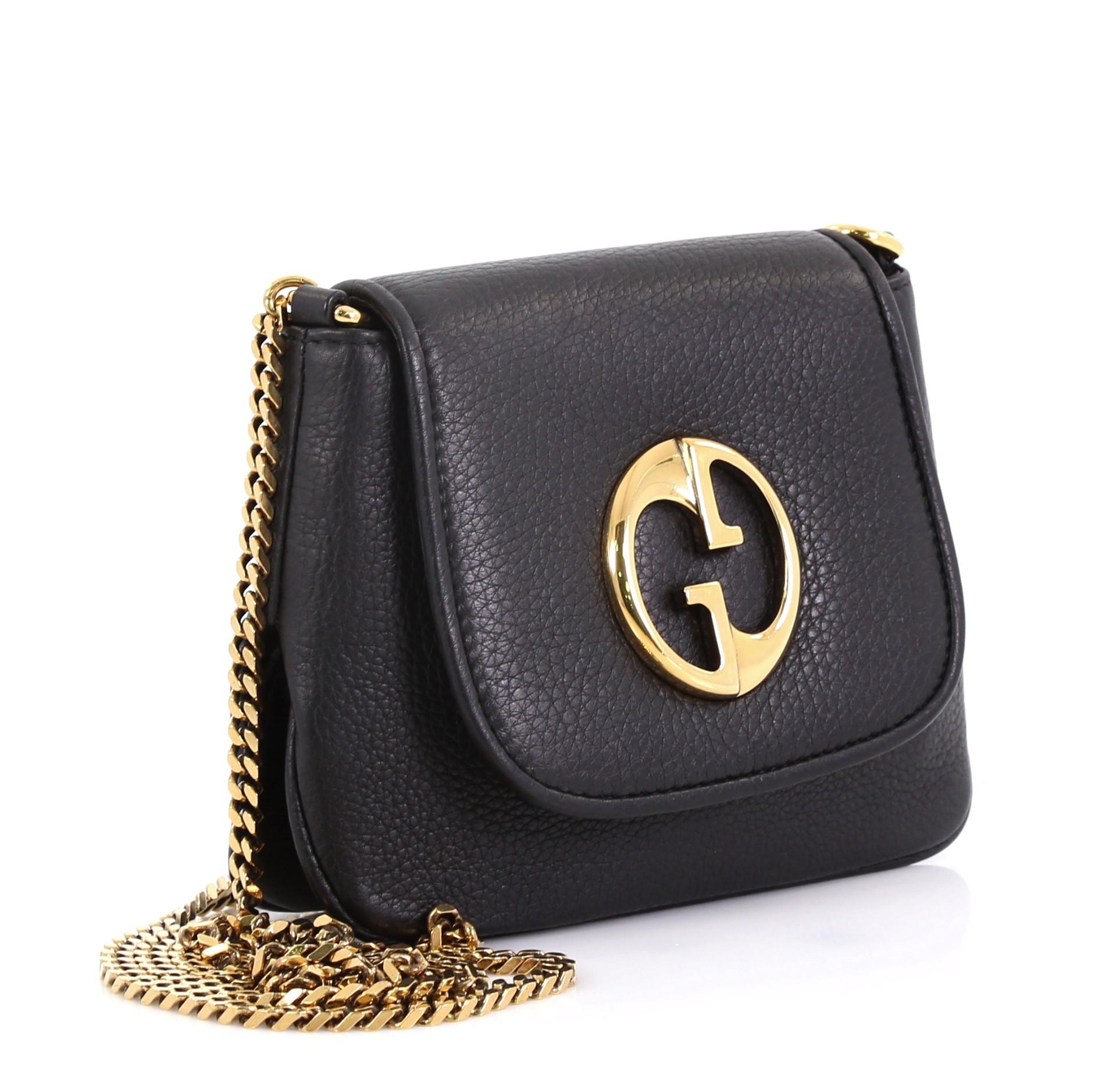 This Gucci 1973 Chain Shoulder Bag Leather Small, crafted in black leather, features classic double G emblem detail, chain link strap, and gold-tone hardware. Its magnetic snap closure opens to a beige microfiber interior with slip pocket.