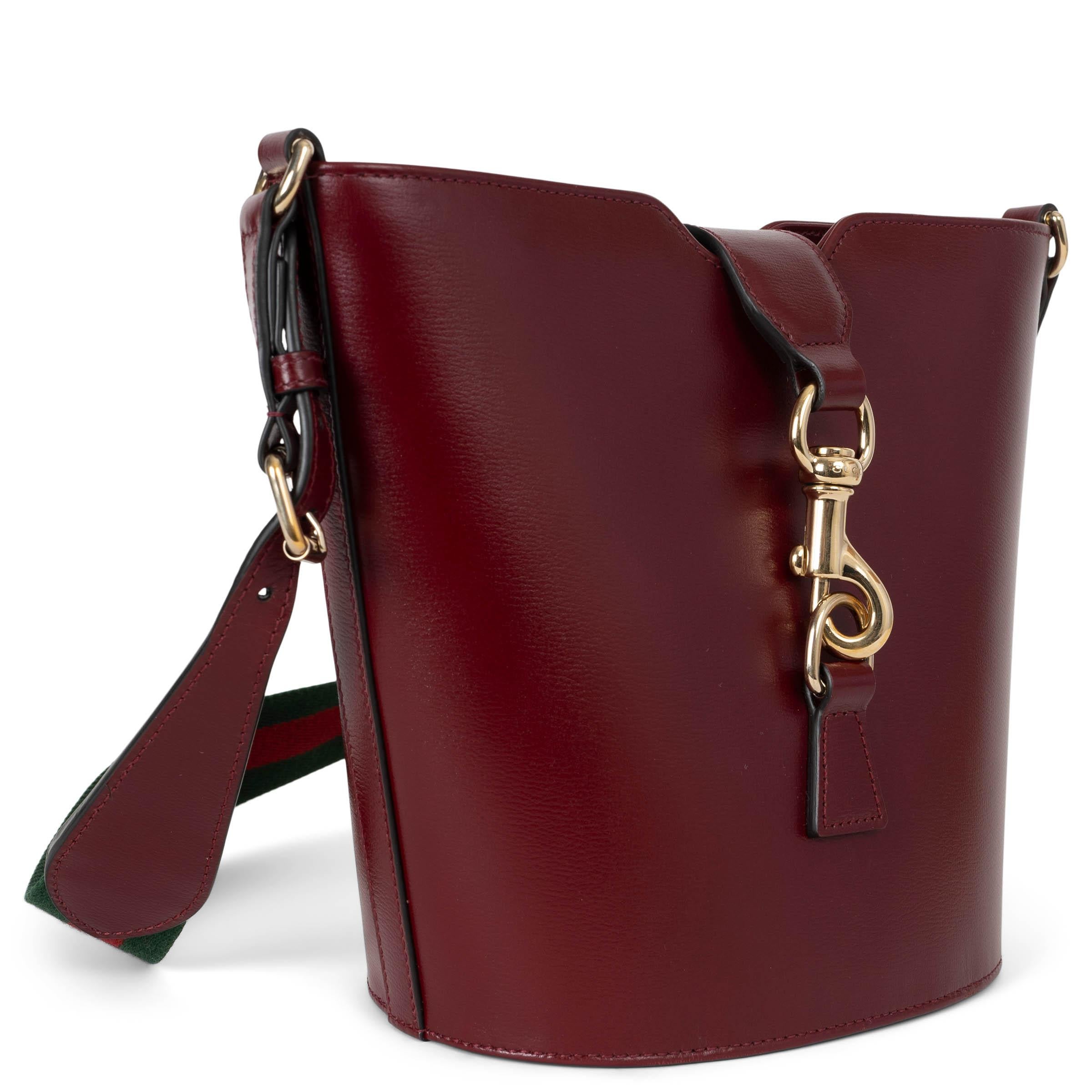 Este bolso bandolera mini bucket 100% auténtico de Gucci en piel roja Rosso Ancora combina el estilo clásico con un toque moderno. Diseñada con un fondo ovalado, lleva una correa ajustable de piel y lona para un uso versátil. El bolso se cierra con