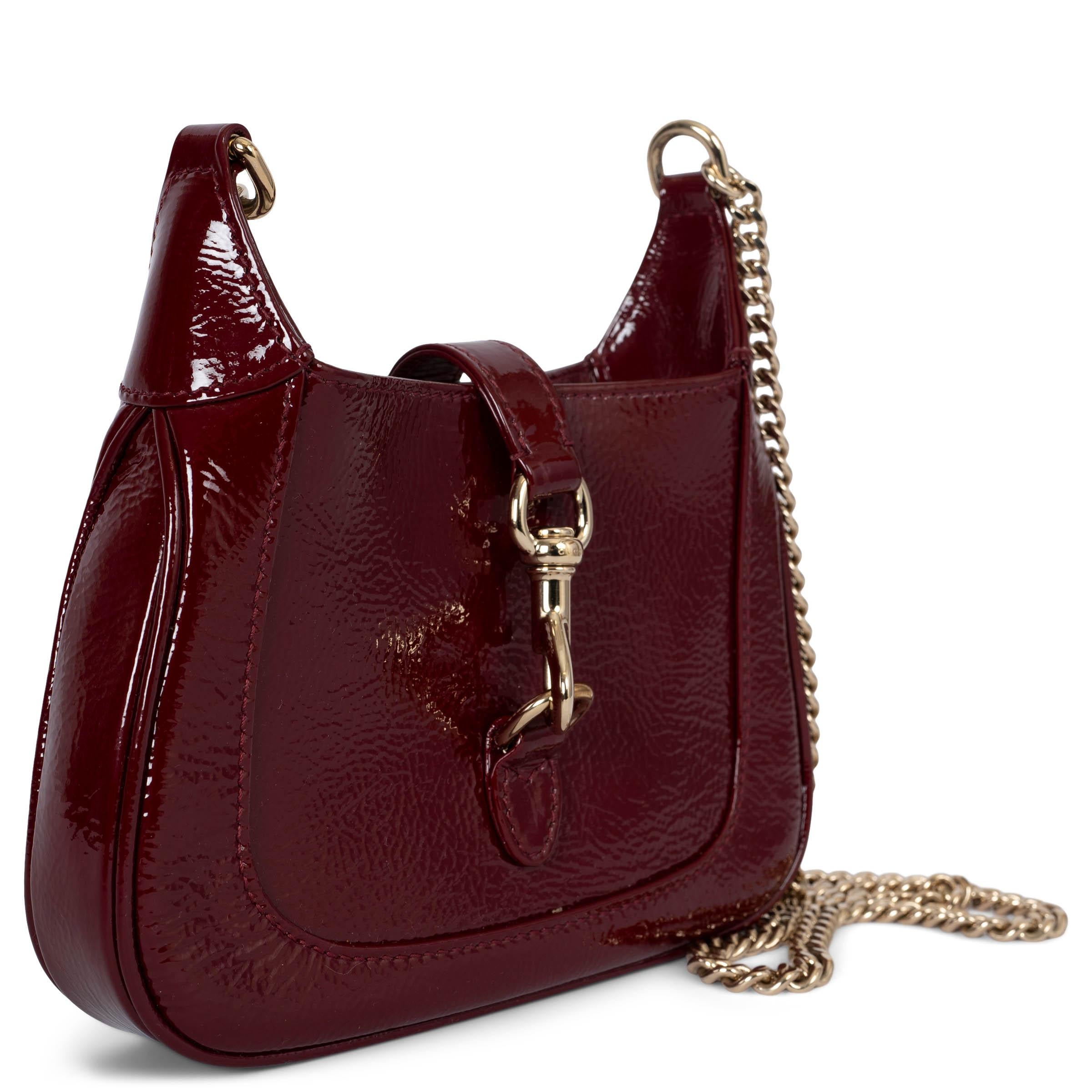 This 100% authentic Gucci Jackie Notte Mini shoulder bag in Rosso Ancora textured patent leather is a sophisticated and compact statement piece. It features a light gold-tone chain strap adorned with GUCCI lettering and a dog-hook closure for a