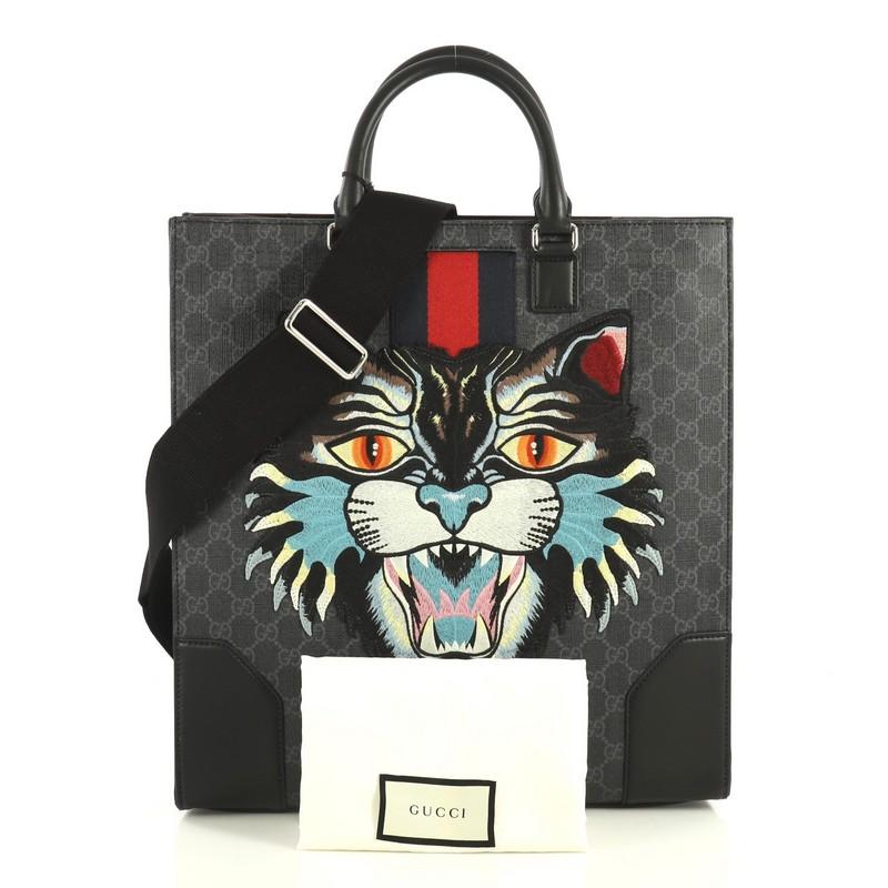 This Gucci Angry Cat Convertible Web Tote GG Coated Canvas Tall, crafted in black GG coated canvas, features dual rolled handles, web with angry cat detail, and silver-tone hardware. Its magnetic closure opens to a black fabric interior with zip and