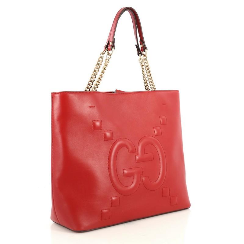 This Gucci Apollo Tote GucciGhost Embossed Leather Large, crafted in red embossed leather, features dual chain link straps with leather pads and gold-tone hardware. Its magnetic closure opens to a neutral microfiber interior with zip and slip