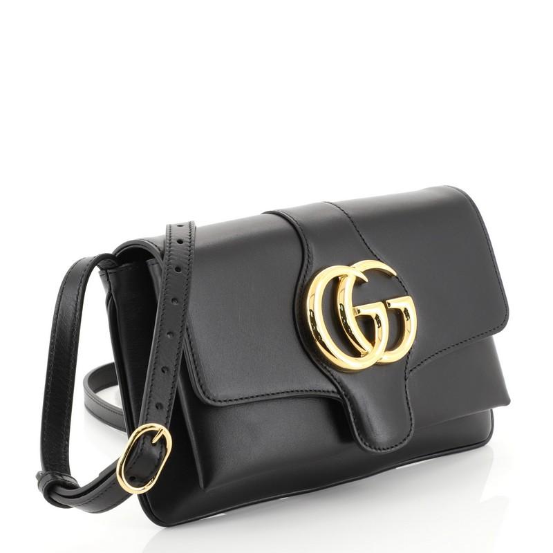 This Gucci Arli Shoulder Bag Leather Small, crafted from black leather, features an adjustable leather strap, flap top with GG logo, and gold-tone hardware. Its magnetic snap closure opens to a pink fabric interior with zip pocket. 

Estimated