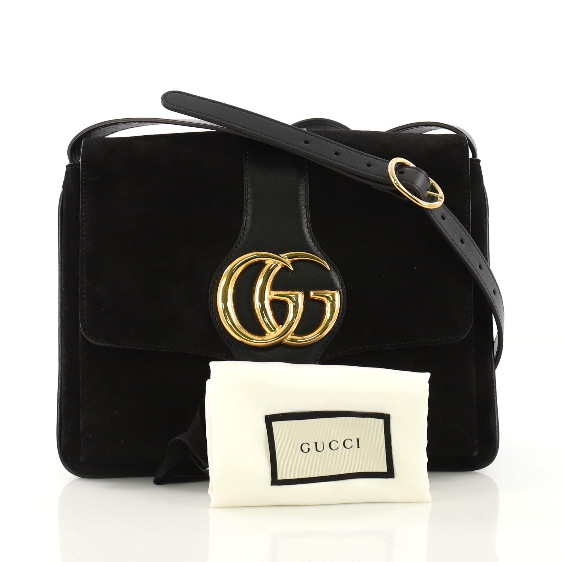 This Gucci Arli Shoulder Bag Suede with Leather Medium, crafted from black suede with leather, features an adjustable leather strap, flap top with GG logo, and gold-tone hardware. Its magnetic snap closure opens to a pink fabric interior with zip
