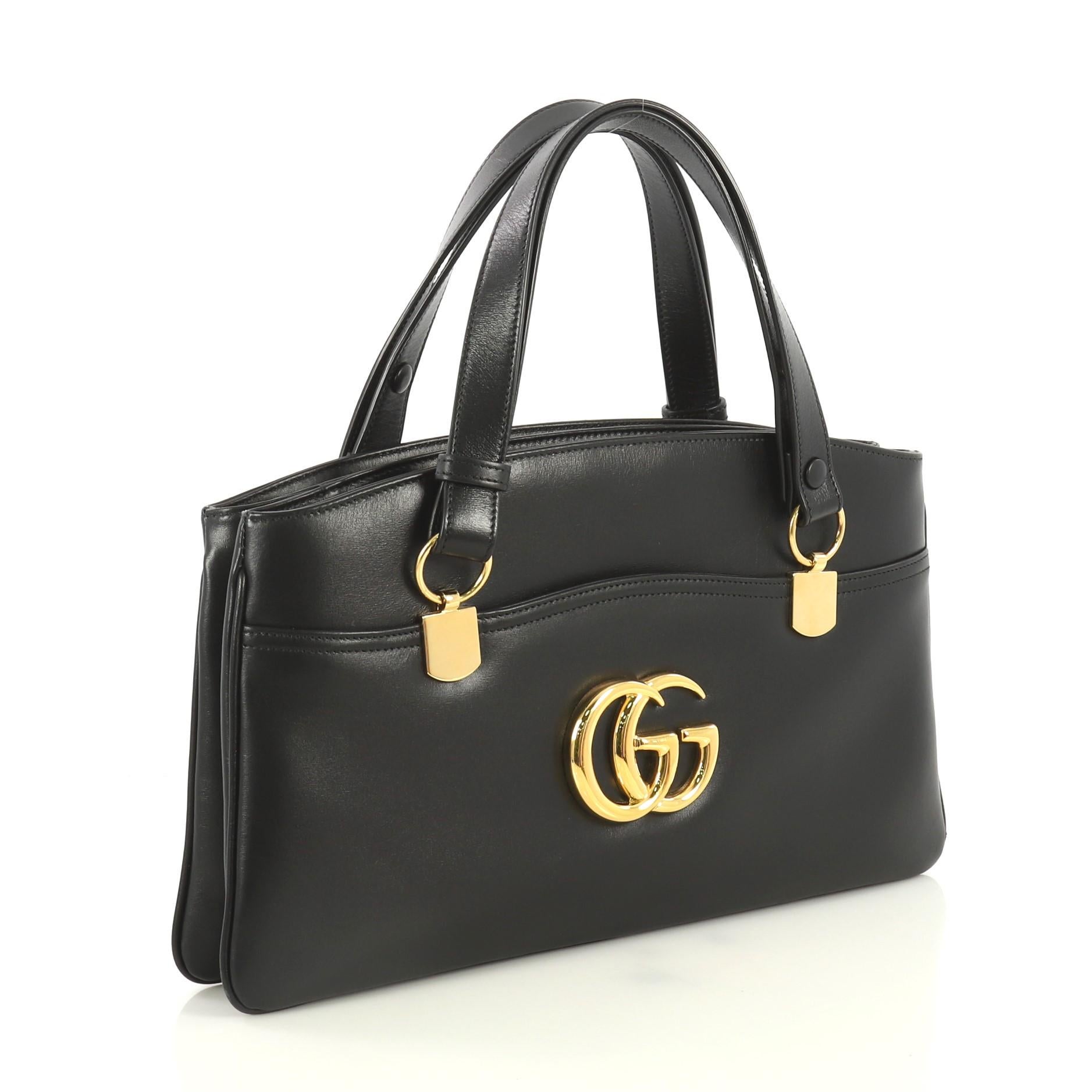 This Gucci Arli Top Handle Bag Leather Large, crafted from black leather, features dual leather handles, GG emblem on front, exterior front and back open pockets, two gussets, and gold-tone hardware. Its zip closure opens to a pink fabric interior