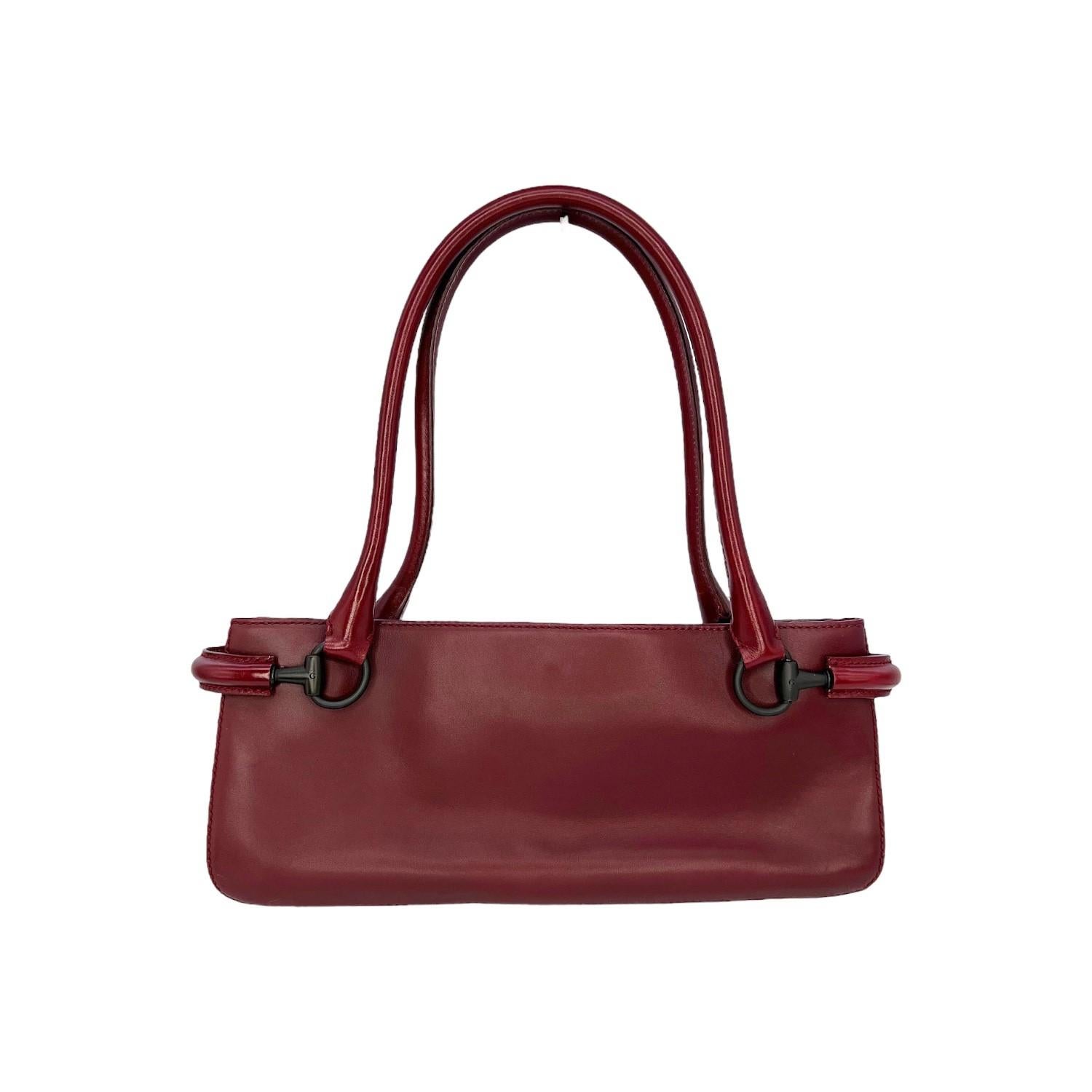 This Gucci Baguette Shoulder Bag is finely crafted of a burgundy leather exterior with matte black hardware features. It has dual rolled leather shoulder straps. It has a magnetic snap closure that opens up to a Gucci jacquard fabric interior with a