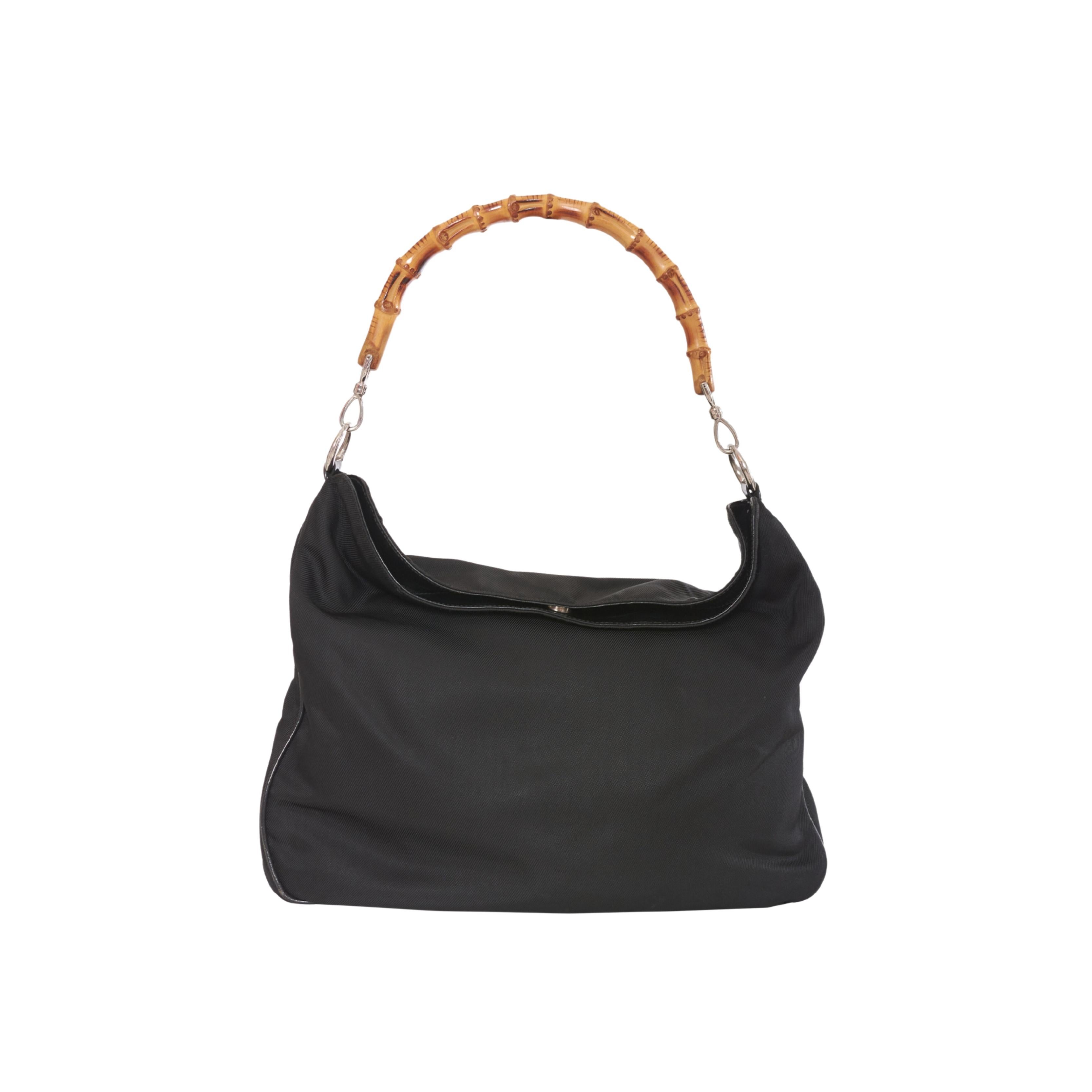 Made of high-quality canvas with glossy black leather trim, the iconic bamboo bag by Gucci features a beautiful hand-woven bamboo handle that lends an exotic and natural touch to its aesthetic. 
The bag's snap-button closure is easy to use. Inside