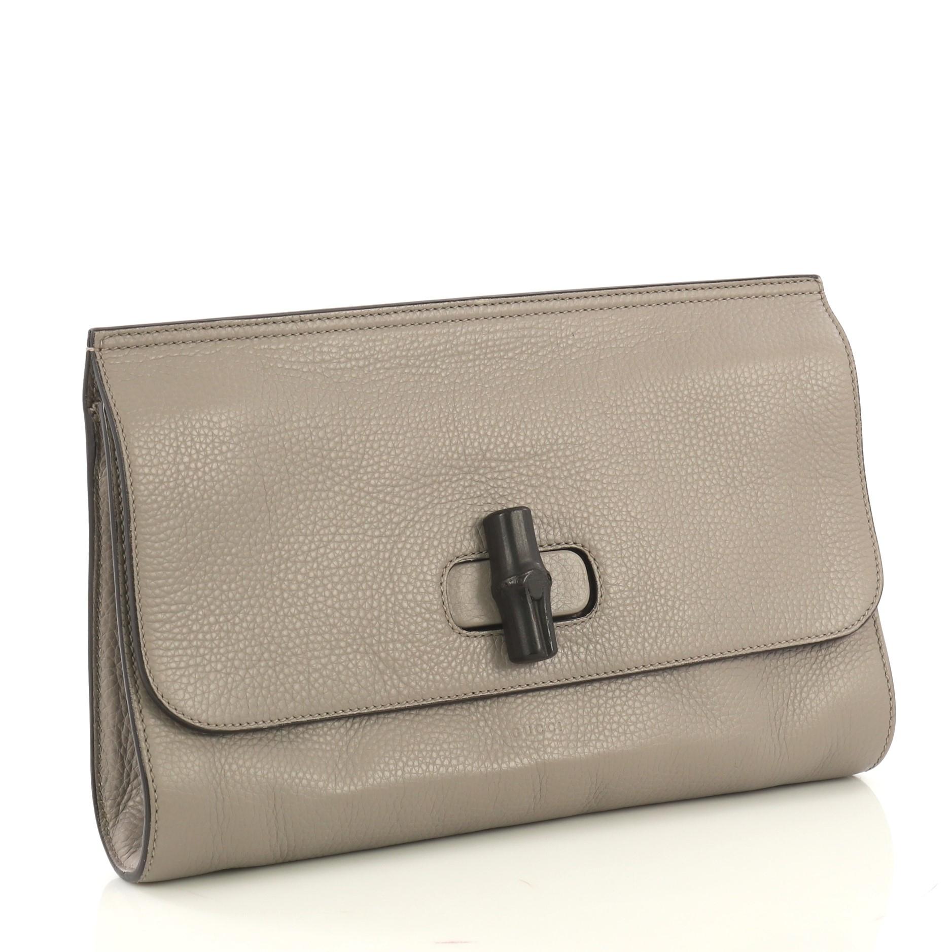This Gucci Bamboo Daily Clutch Leather, created in gray leather, features flap closure with dark lacquered bamboo detail, back slip pocket and silver-tone hardware. Its turn-lock closure opens to a light pink printed fabric interior with zip and