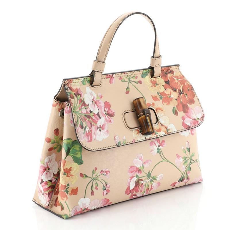 This Gucci Bamboo Daily Top Handle Bag Blooms Print Leather Small, crafted from pink printed leather, features multicolor feminine blooms prints, a single looped leather handle, front flap with bamboo twist-lock closure, side magnetic snaps and aged