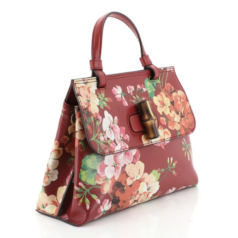 This Gucci Bamboo Daily Top Handle Bag Blooms Print Leather Small, crafted from red Blooms printed leather, features feminine blooms prints, a single looped leather handle, front flap with bamboo twist-lock closure, and aged silver-tone hardware.