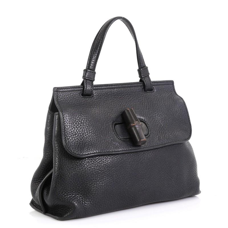 This Gucci Bamboo Daily Top Handle Bag Leather Small, crafted from black leather, features a flat top handle and silver-tone hardware. Its flap with bamboo turn-lock closure opens to a neutral printed fabric interior with zip and slip pockets. These