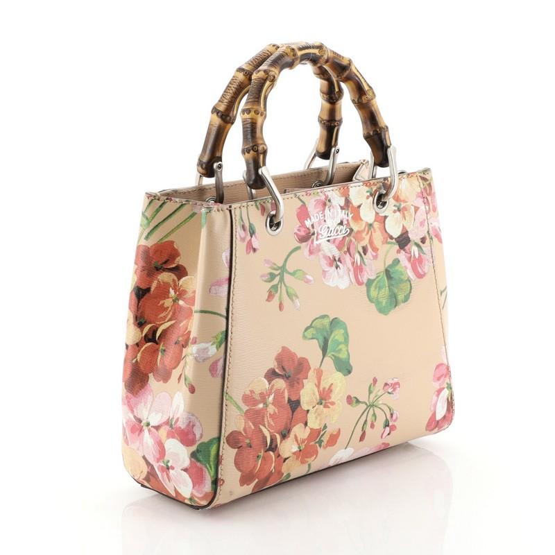 This Gucci Bamboo Shopper Tote Blooms Print Leather Mini, crafted from pink blooms print leather, features sturdy bamboo handles, stamped logo at the front, and aged silver-tone hardware. Its hidden magnetic snap closure opens to a neutral fabric
