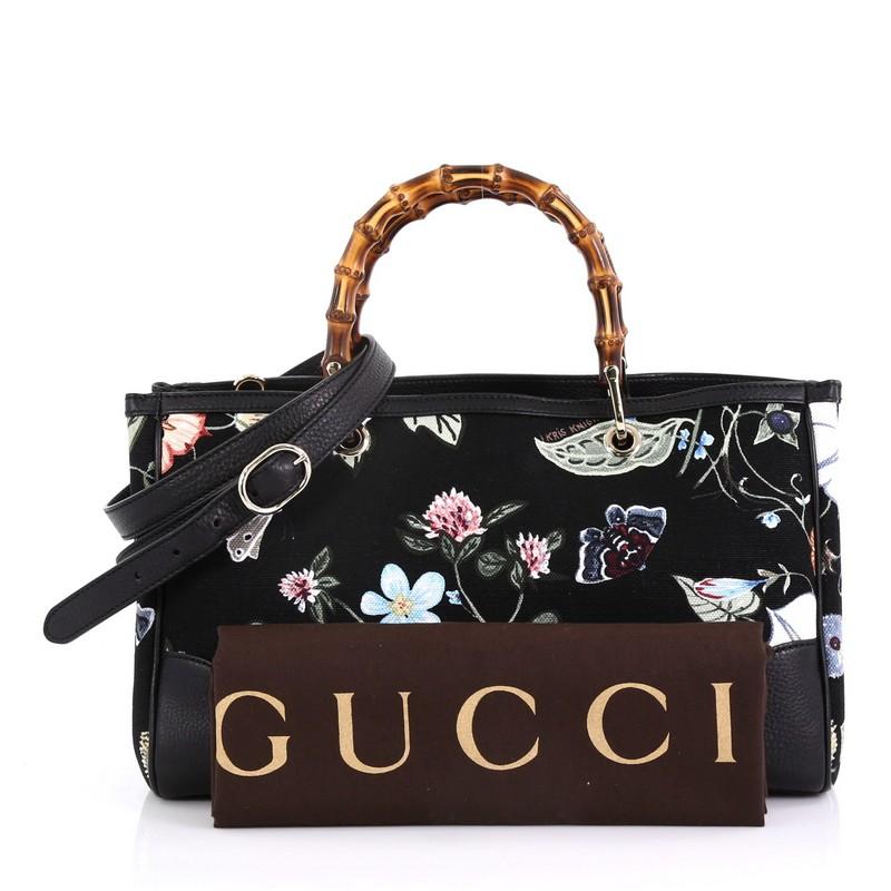 This Gucci Bamboo Shopper Tote Flora Canvas Medium, crafted from black flora canvas, features dual bamboo handles, floral motif, leather trim, and gold-tone hardware. Its magnetic tab closure opens to a beige canvas interior with middle zip